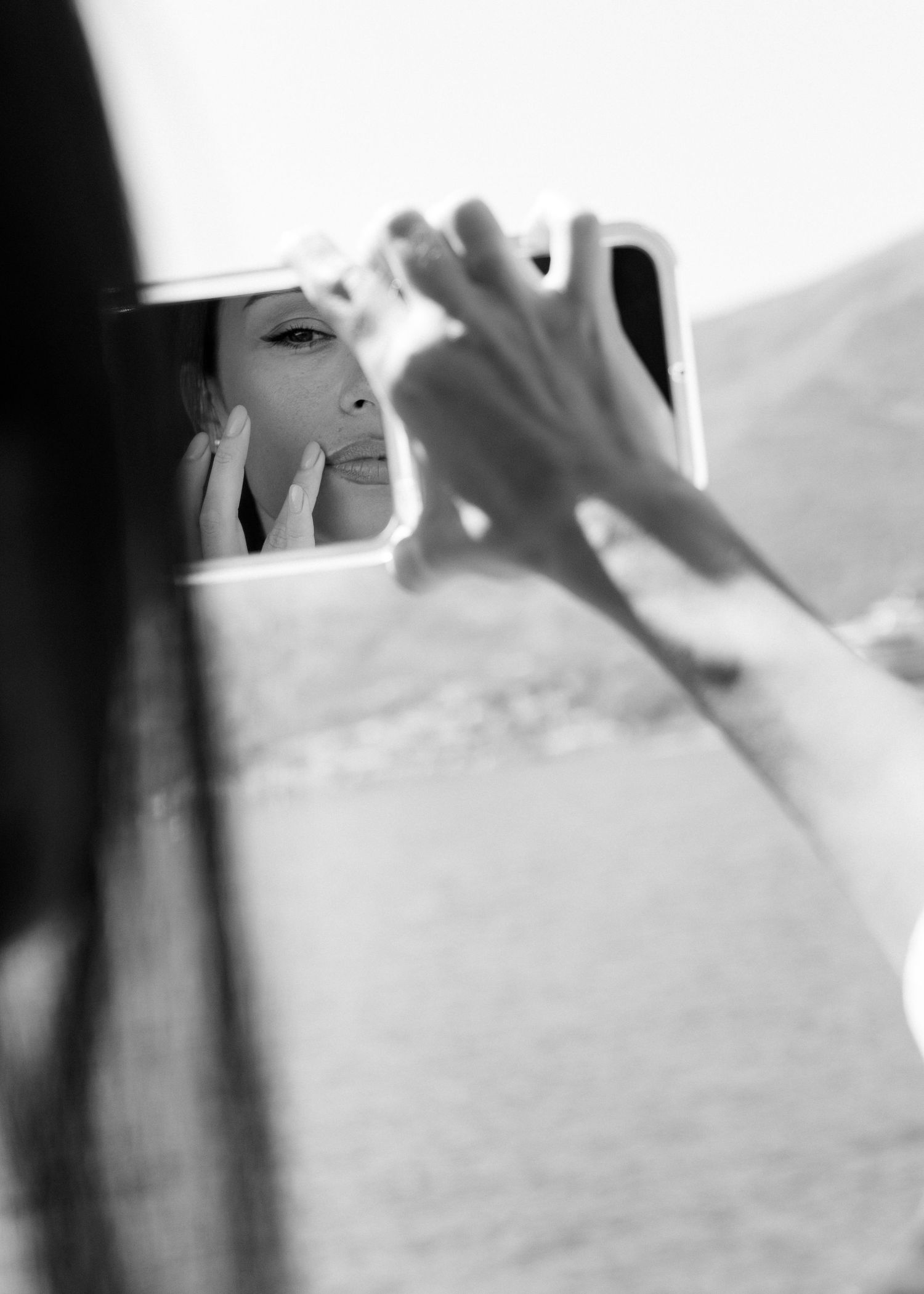 A reflection in a car side mirror shows someone applying makeup while using the mirror as they sit in a vehicle.