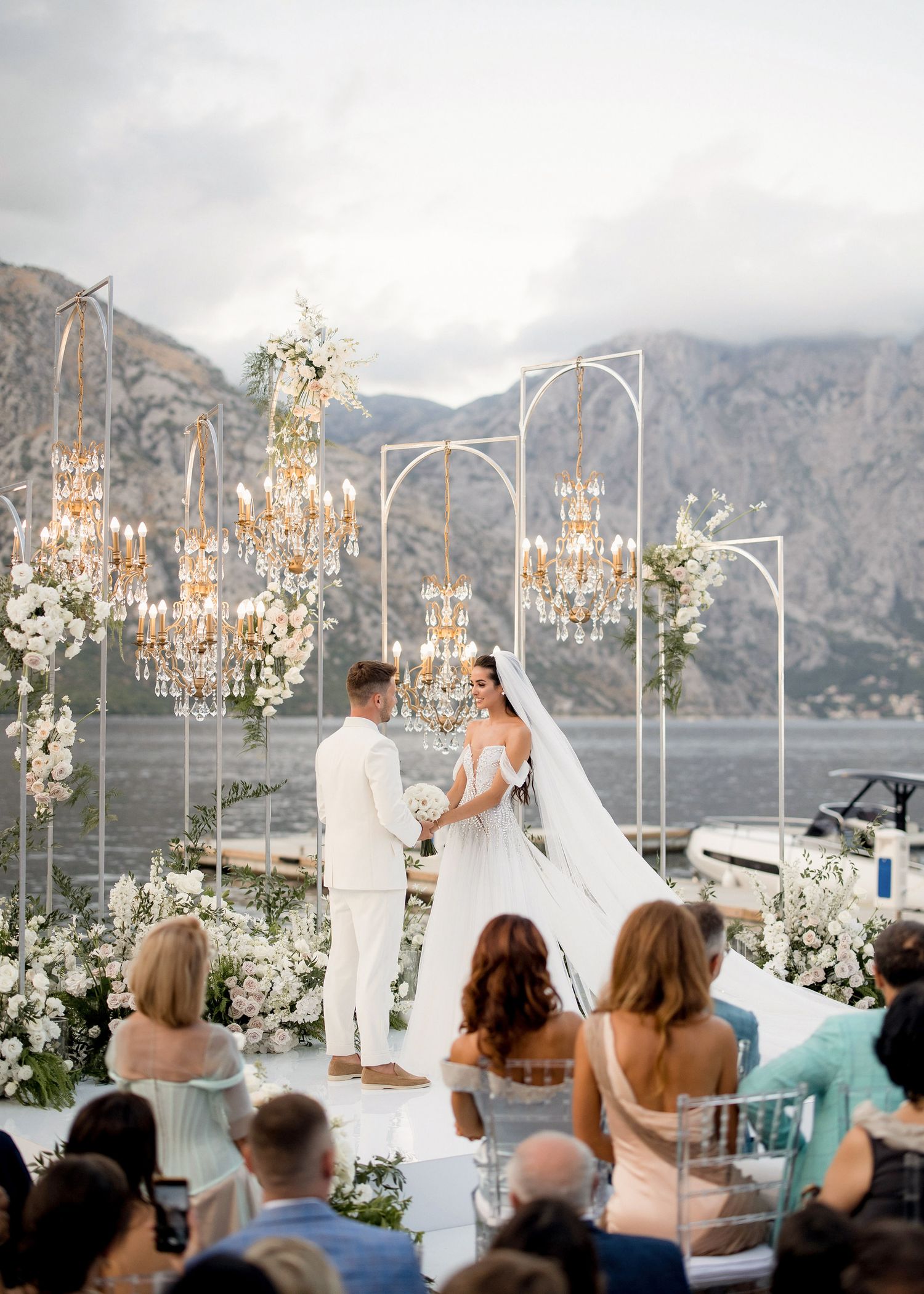 Elegant outdoor wedding ceremony with chandeliers, floral arches, and mountain lake backdrop.