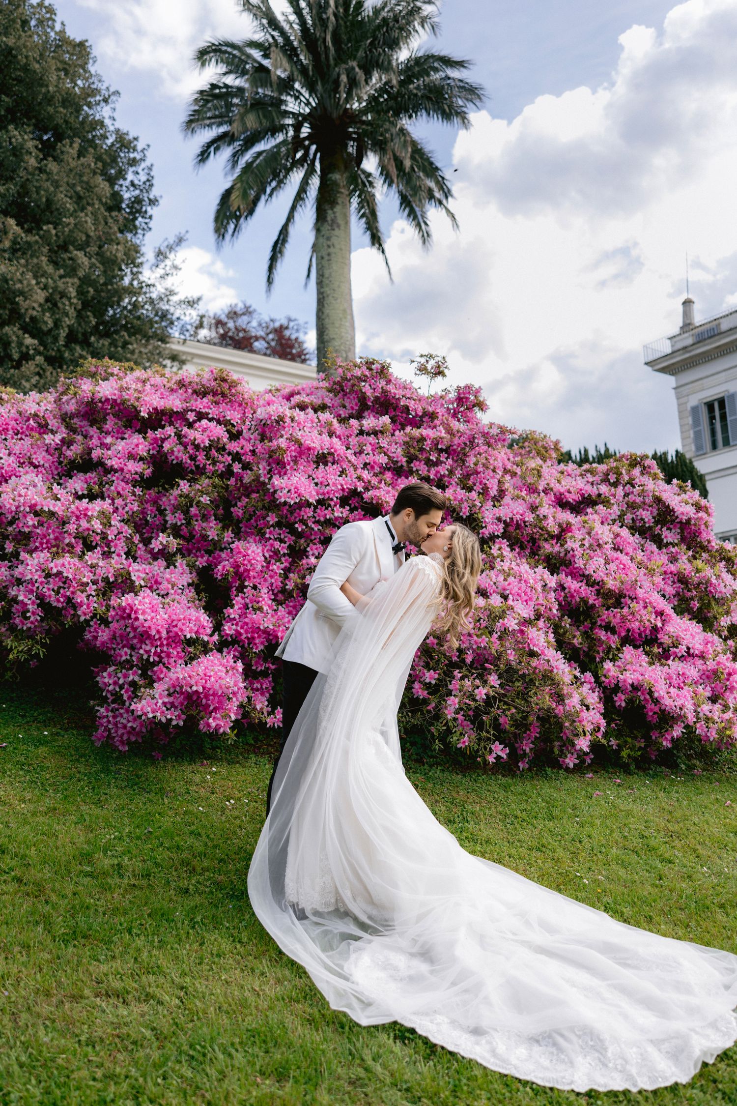 Romantic wedding portrait with flowing dress against vibrant pink bougainvillea and palm tree.