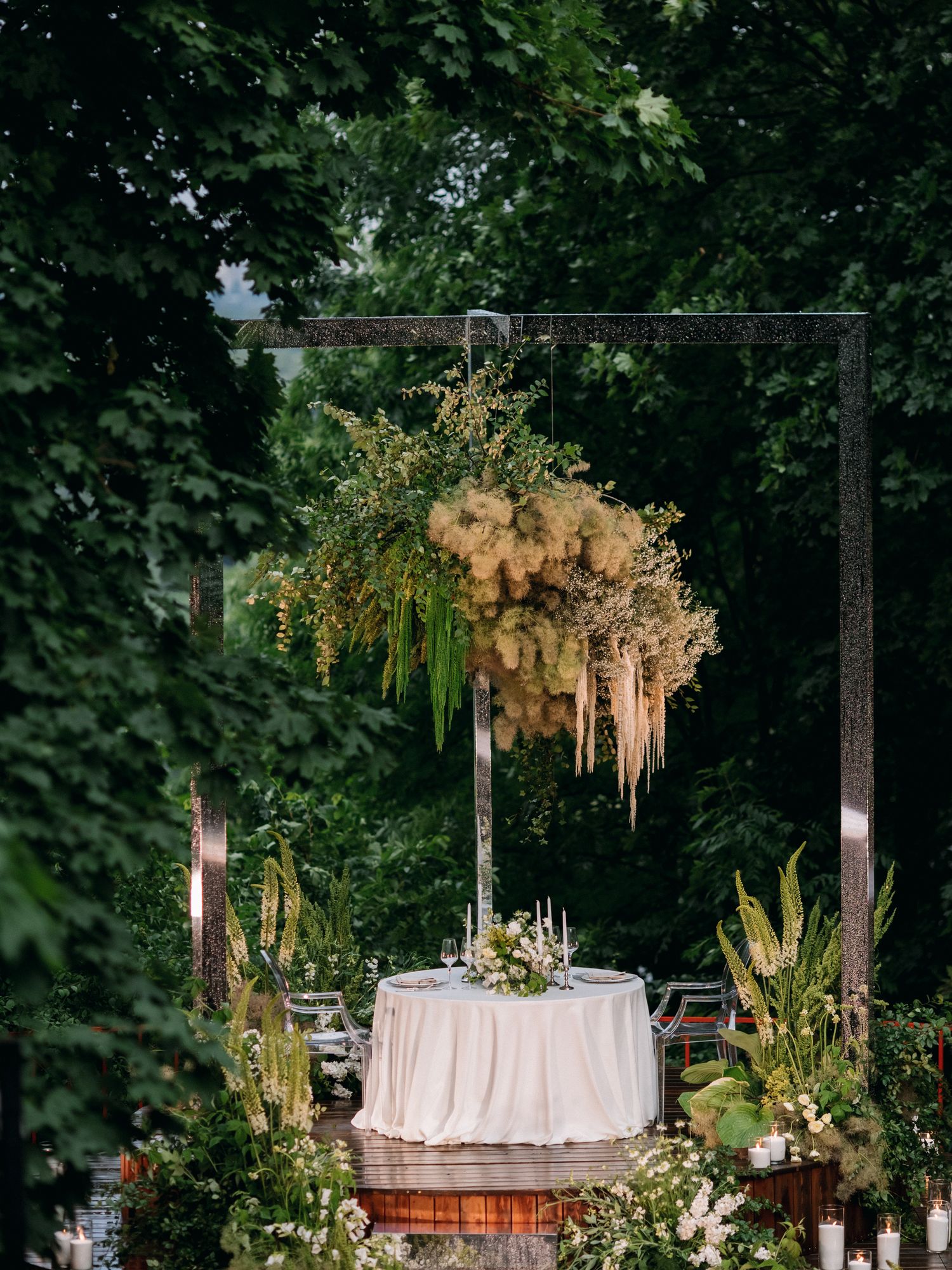 Elegant outdoor table setting with hanging floral arrangement and garden backdrop.