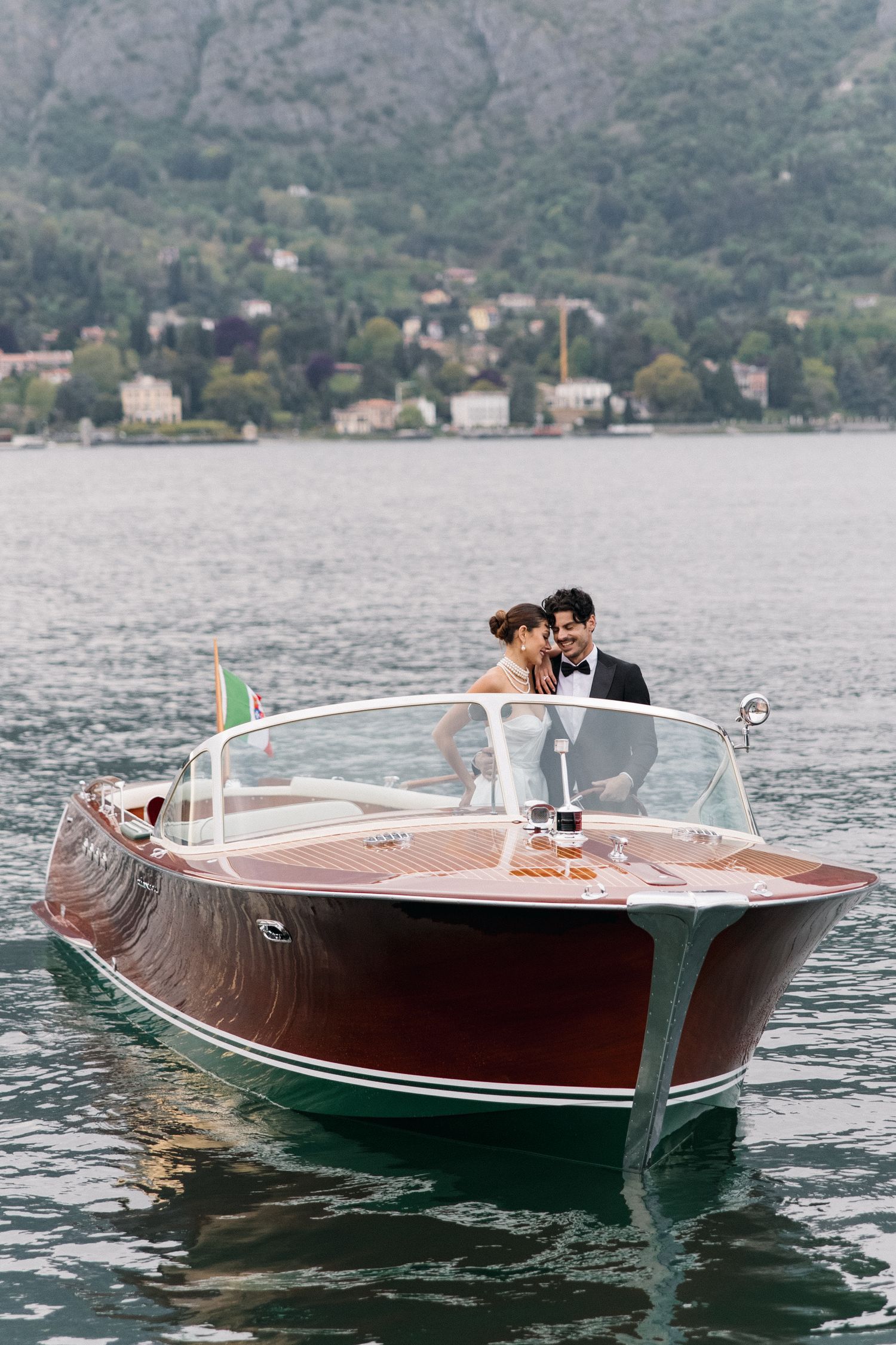 Newlyweds aboard a classic wooden boat cruising on an Italian lake.