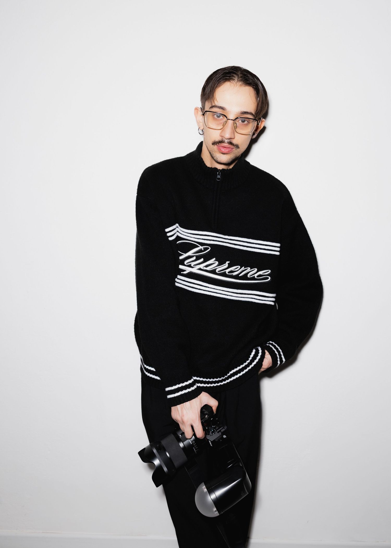 Person in black graphic sweatshirt posing with camera against white background in multiple shots.