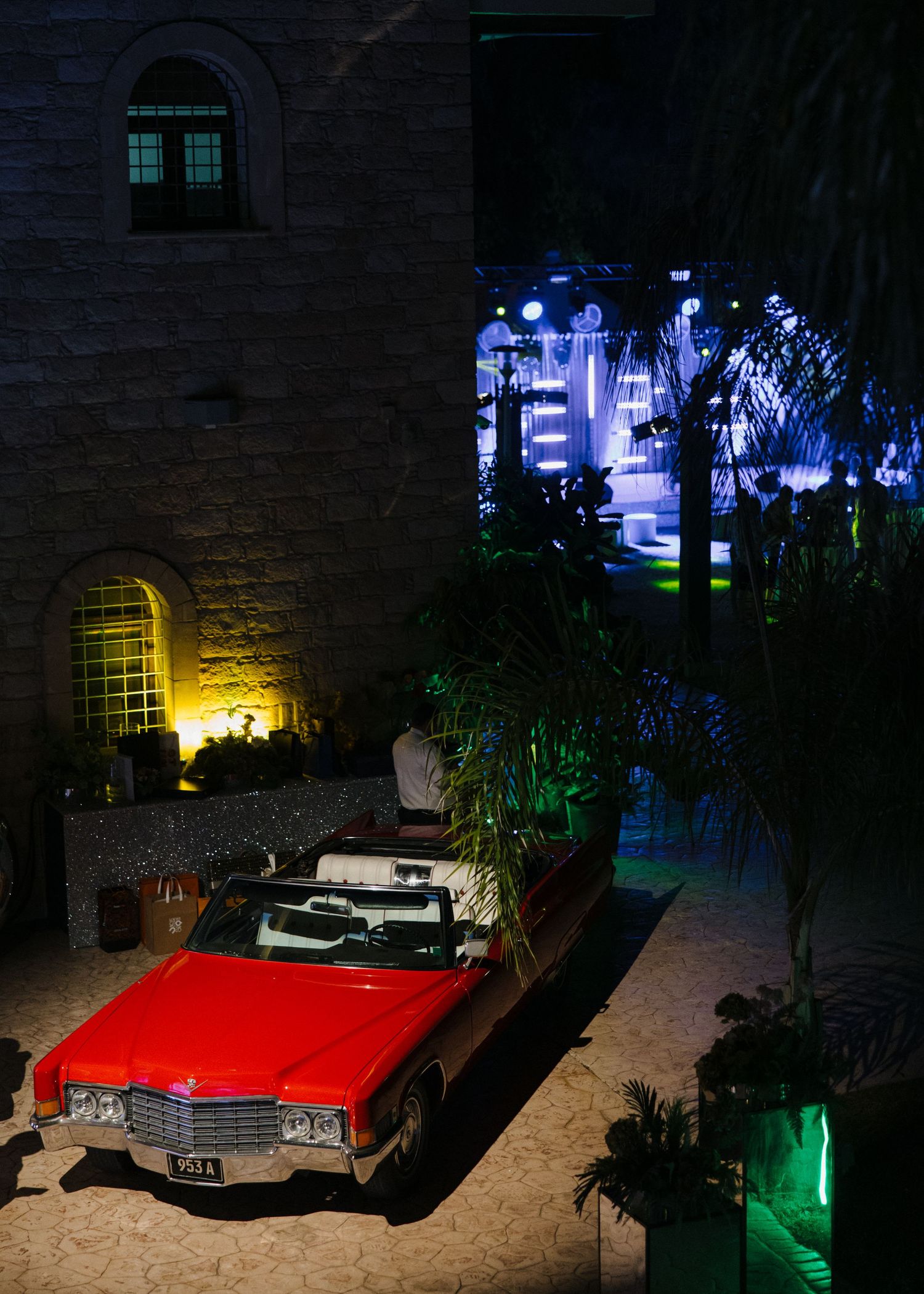 Vintage red convertible car parked near stone walls with atmospheric blue and yellow lighting.