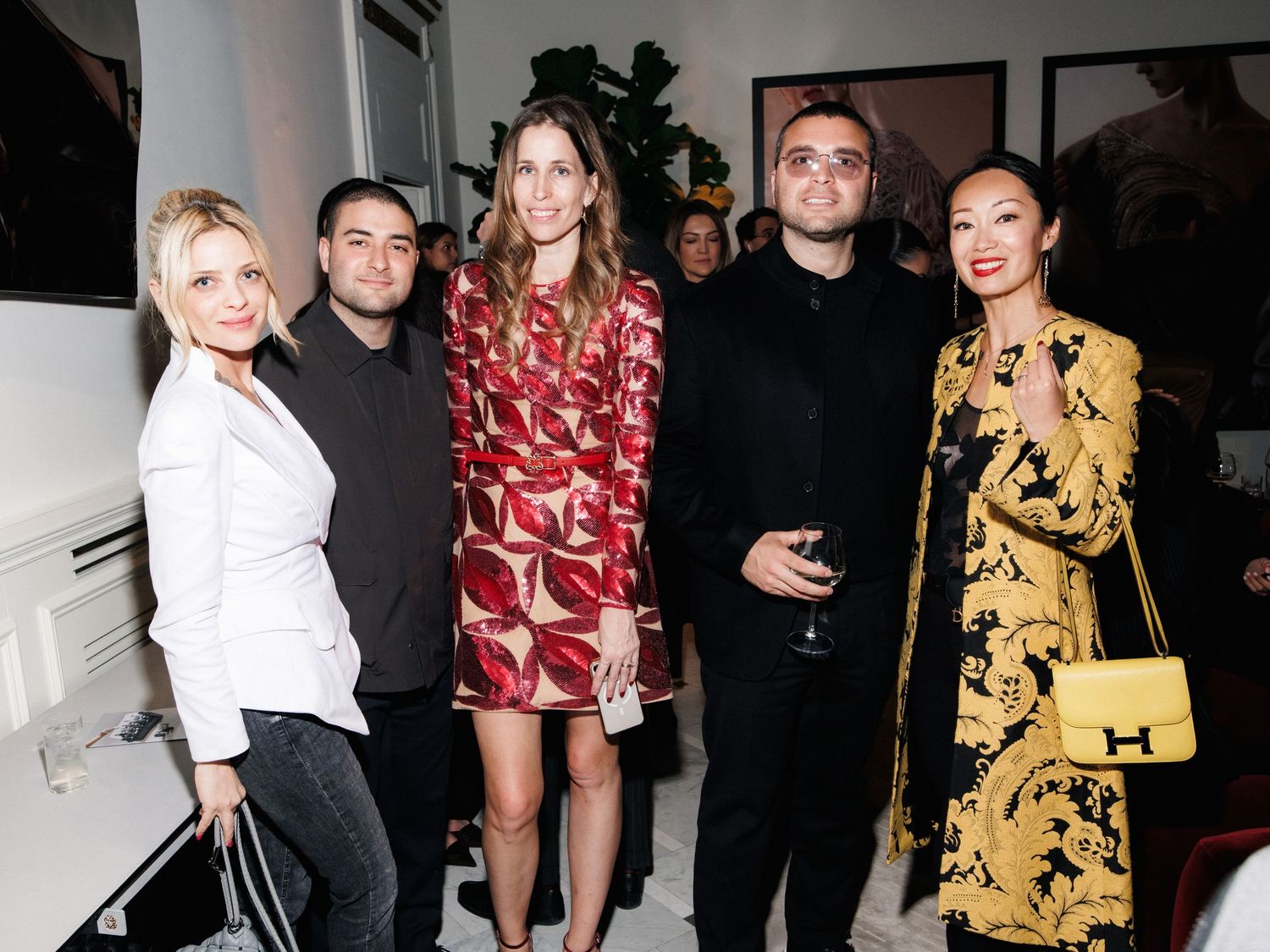 People in formal attire pose together at a social event with dark background and stylish outfits.