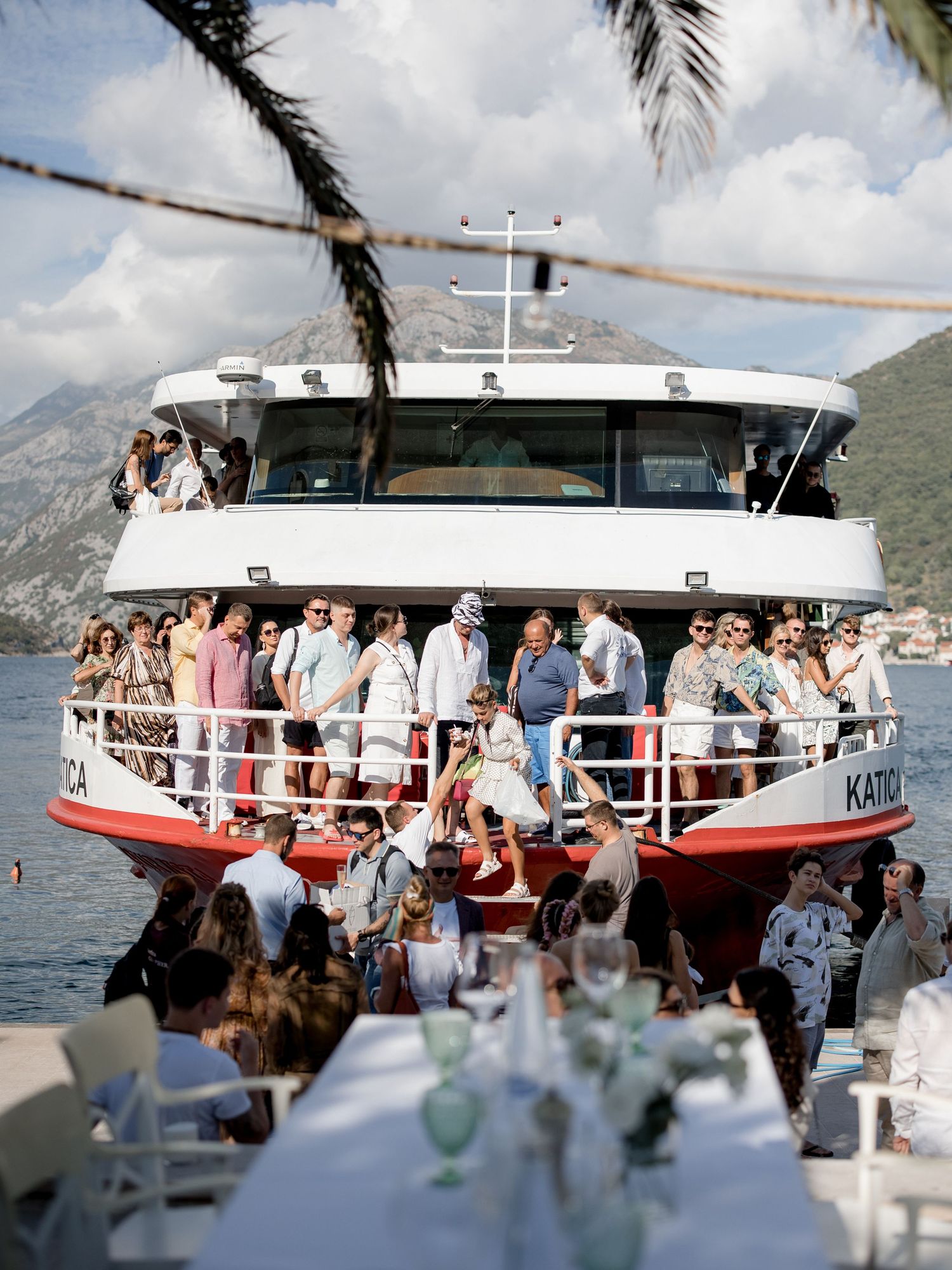 Crowded party boat filled with guests cruising along mountainous coastline.
