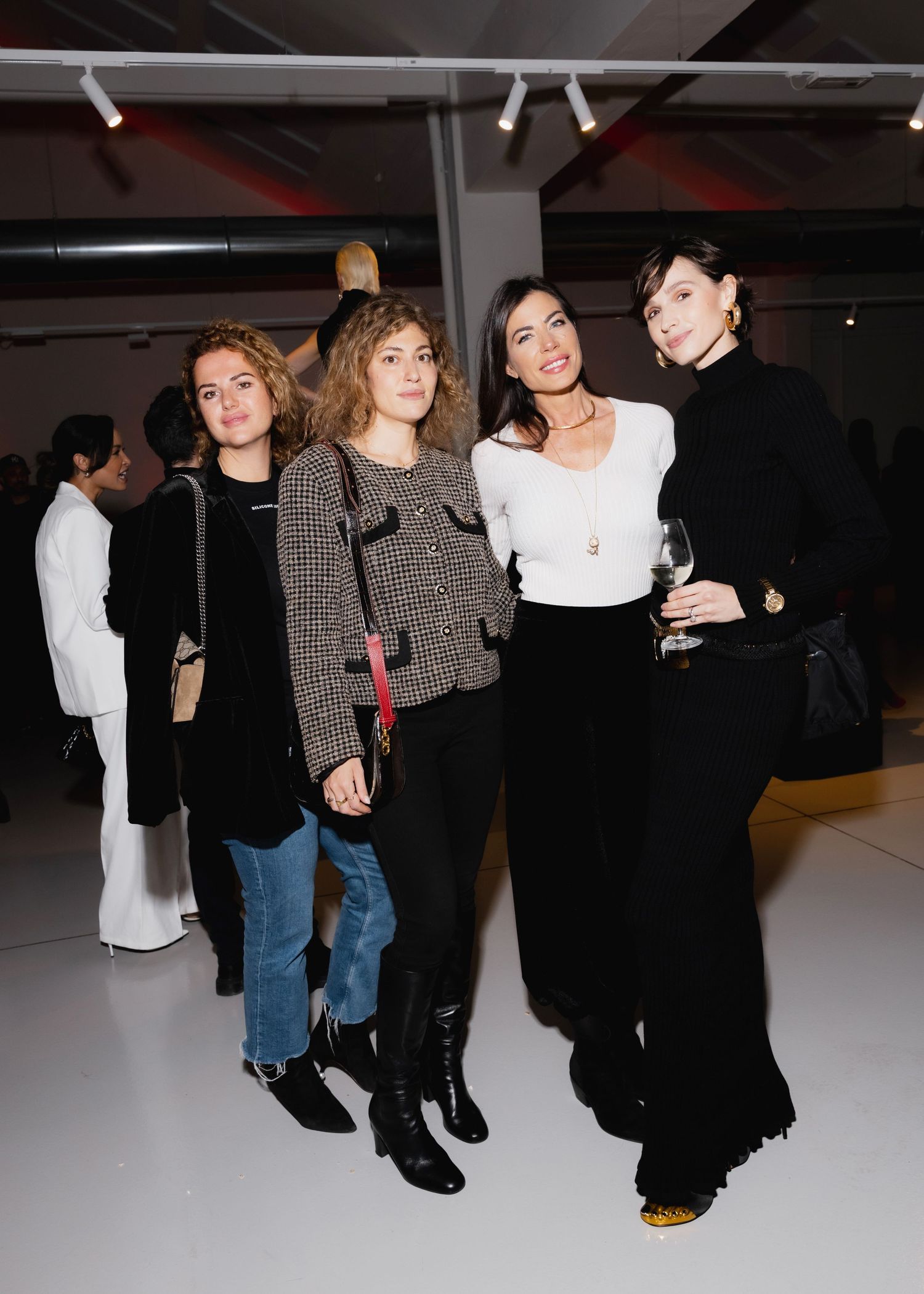 Group of people mingling at an indoor event wearing casual and formal attire in a dimly lit space.