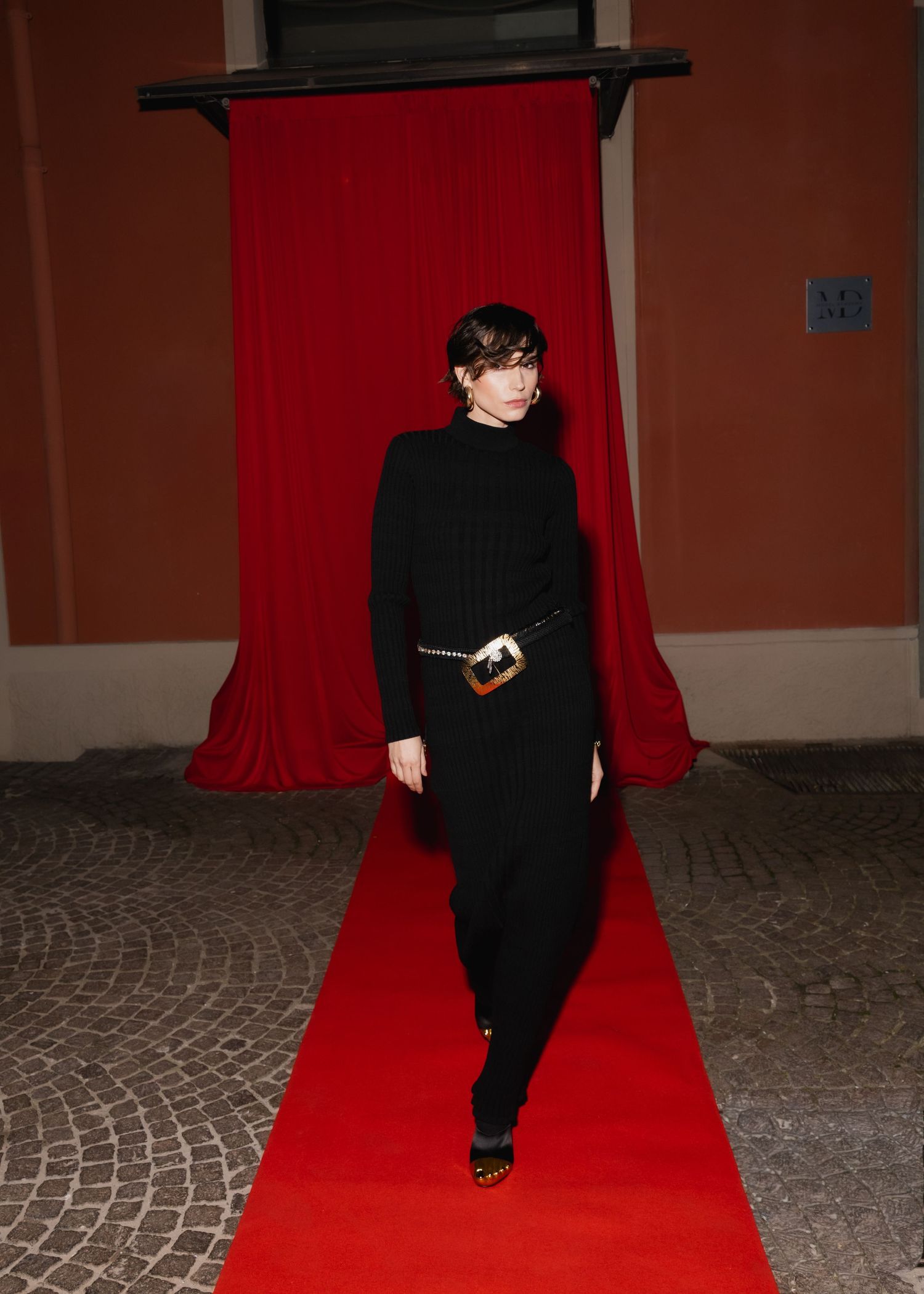 A sequence of photos showing a person in black attire walking across a red carpet on a stone-paved floor.
