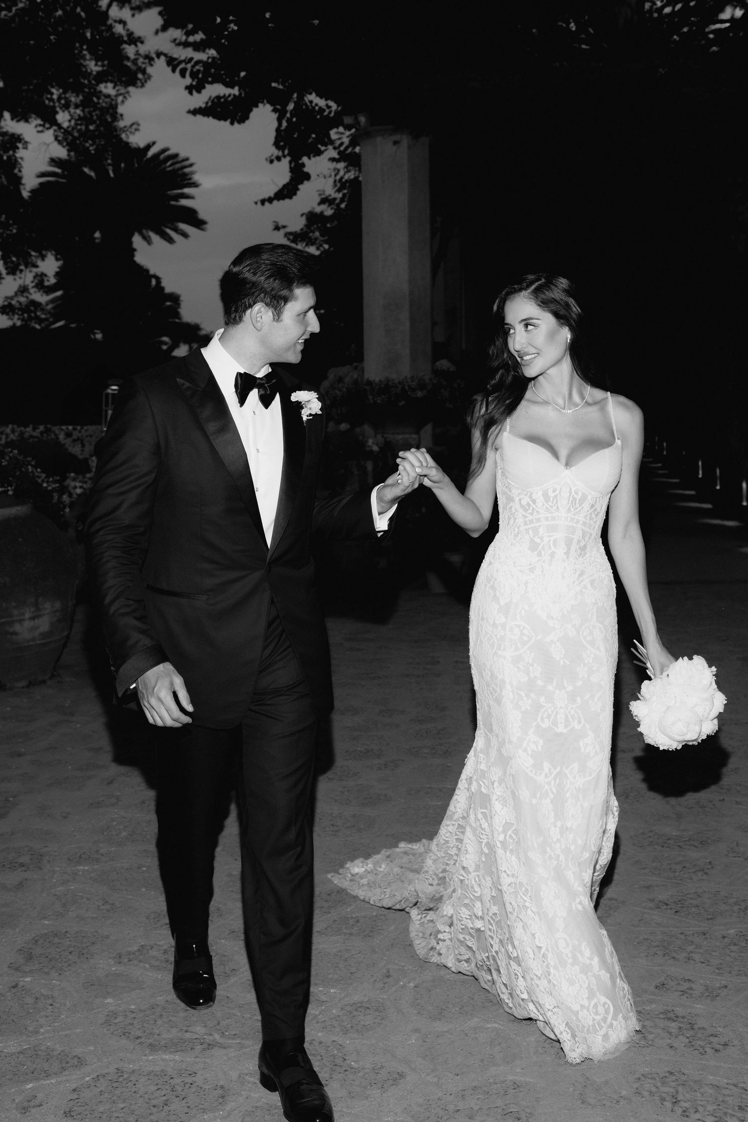 A couple in formal wedding attire walks together during their evening celebration.