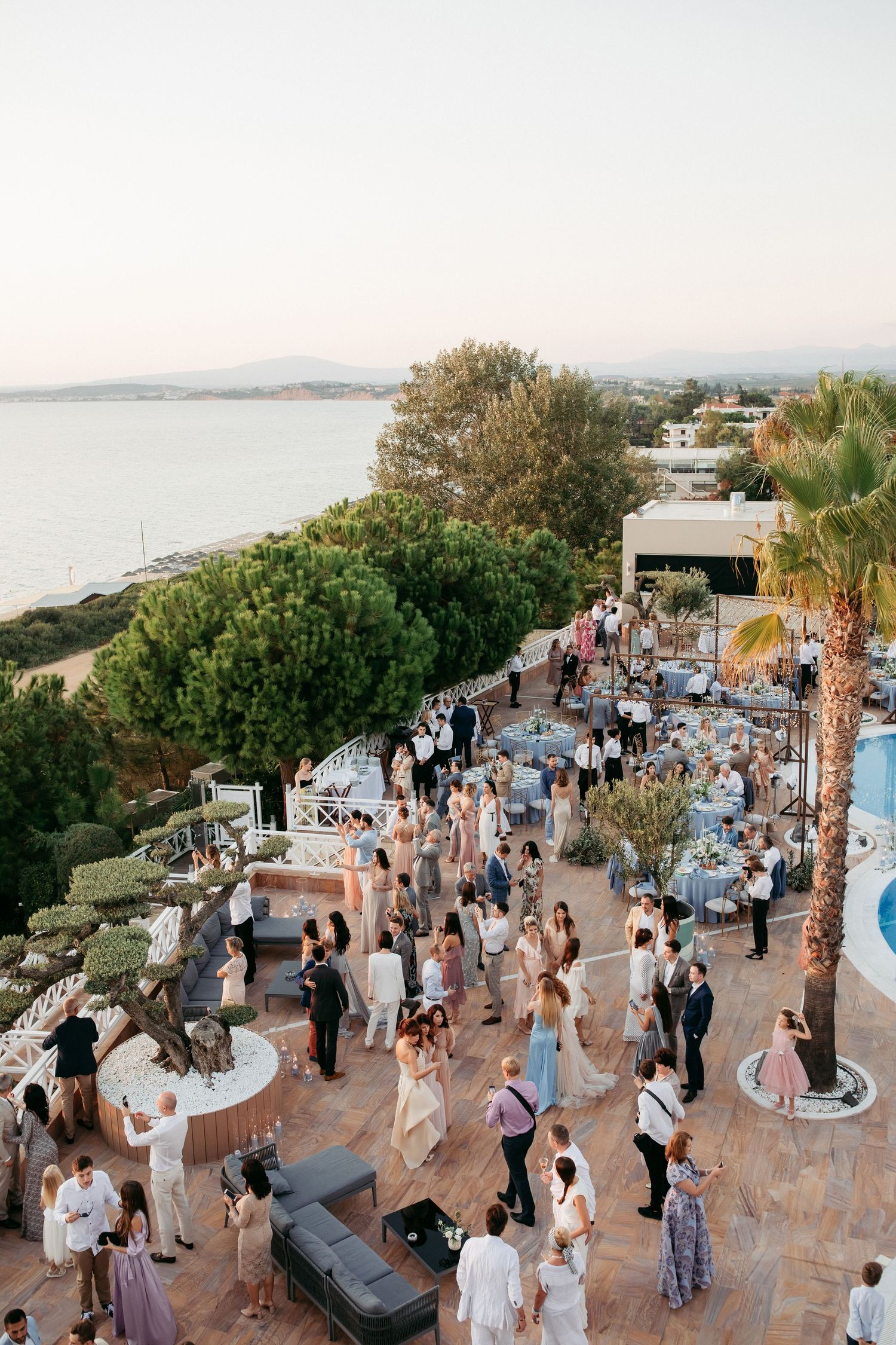 Aerial view of outdoor party venue overlooking coastline with guests mingling on terrace.