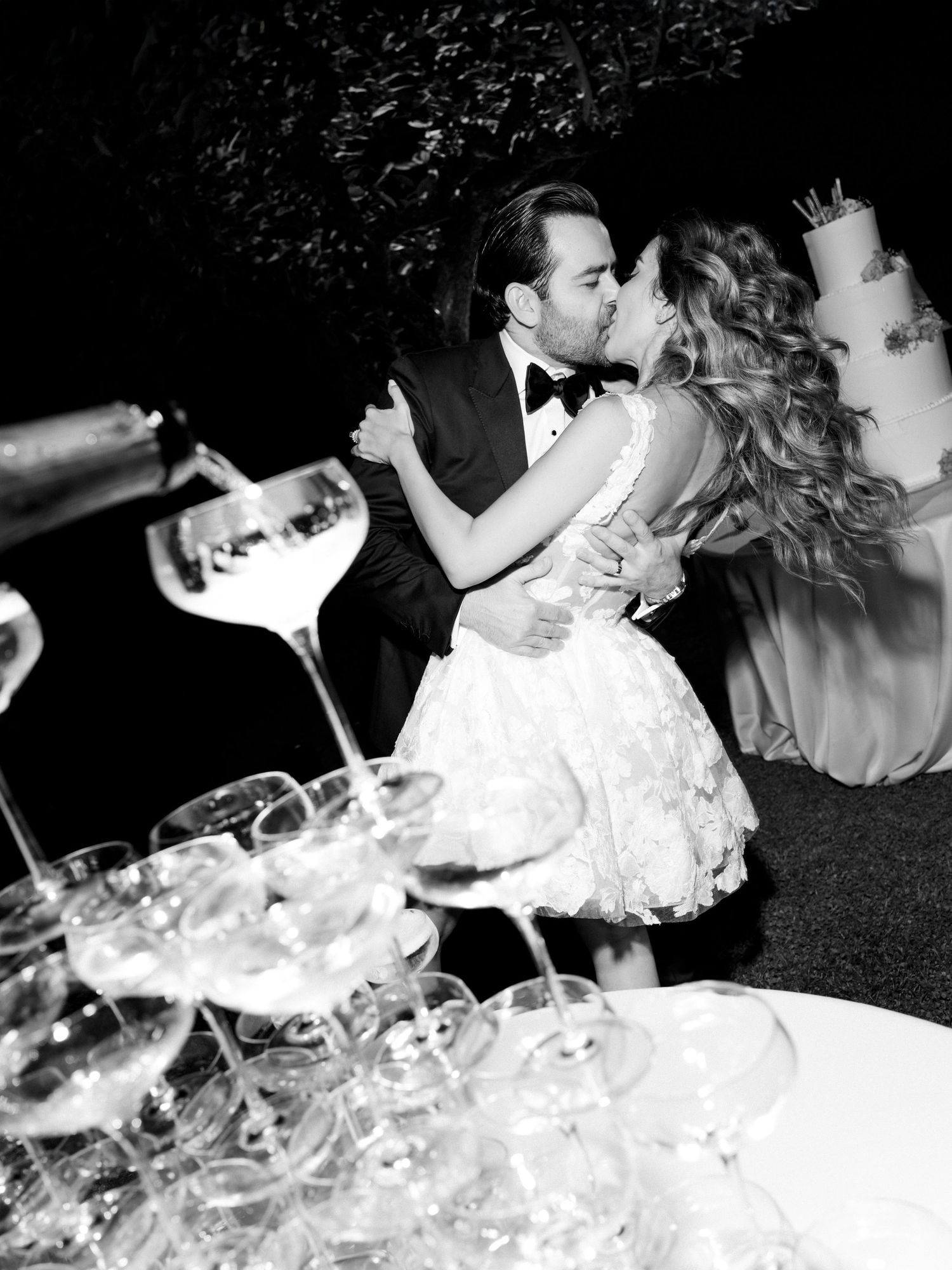 A black and white photo of a wedding celebration with a champagne tower in the foreground during a dance.