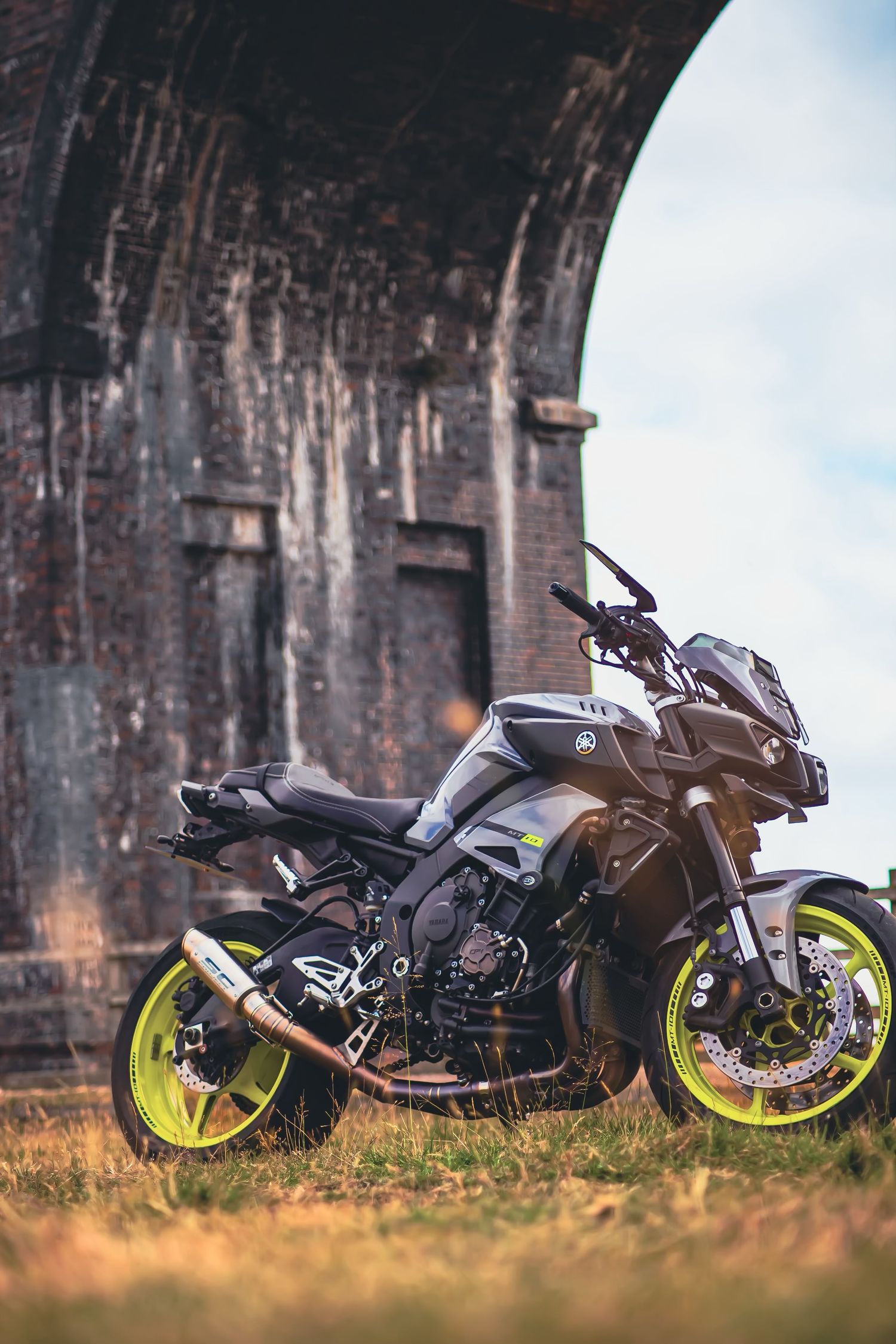Modern sport motorcycle with neon yellow wheels photographed against an old brick wall backdrop.