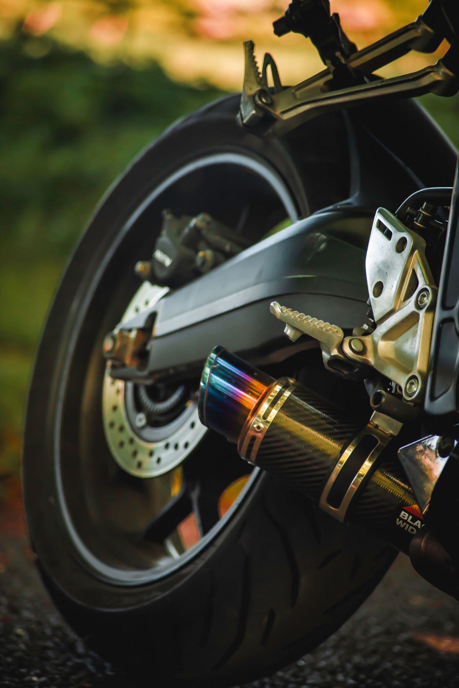 Close-up detail shots of a motorcycle's rear wheel, brake disc, and suspension components in warm lighting.