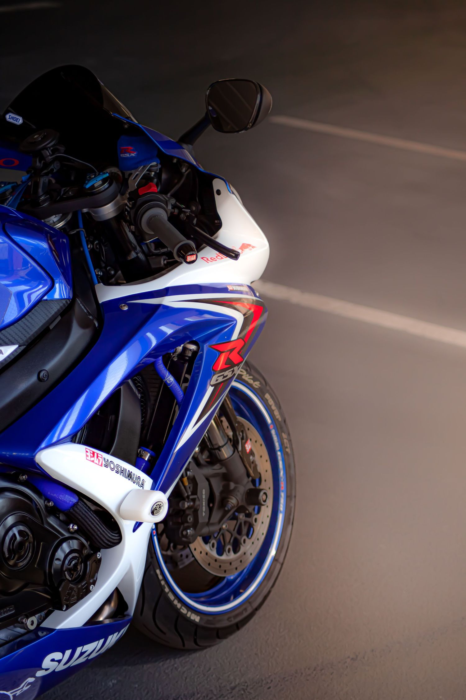 Blue and white Suzuki GSX-R sport motorcycle parked on a road, showcasing its front fairing and wheel detail.