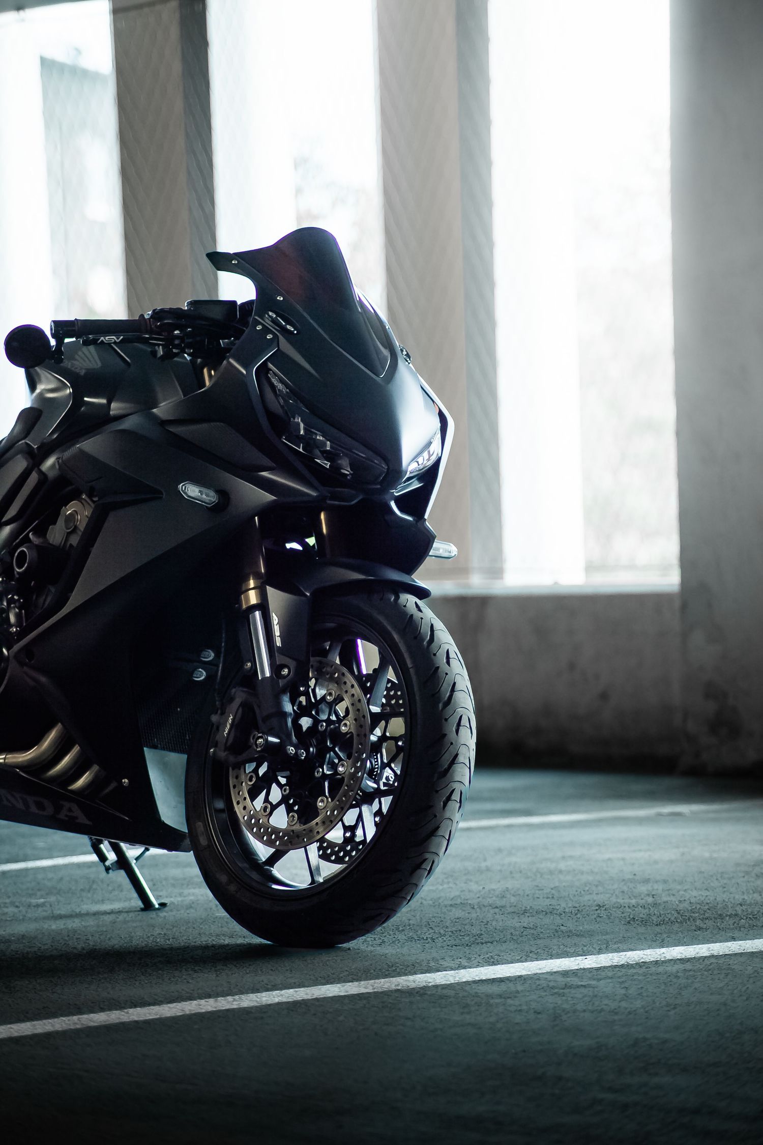 A sleek black sports motorcycle parked in a dimly lit parking garage with dramatic lighting and shadows.