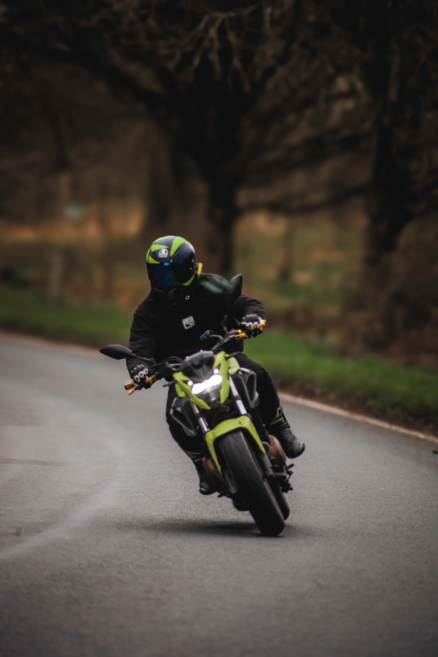 Motorcyclist in black gear rides a neon green sport bike through a curving road on an overcast day.