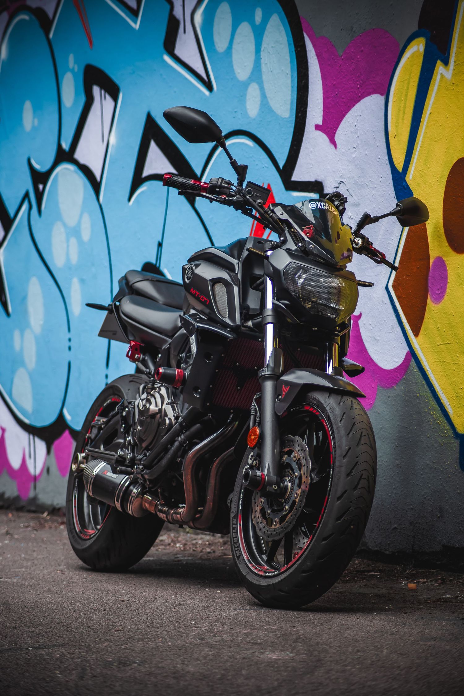 Black sports motorcycle with red accents parked against colorful graffiti wall featuring blue and pink street art.