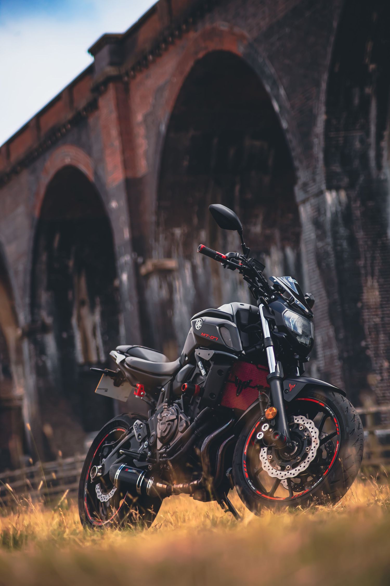 Four modern motorcycles parked in a row against dramatic brick arches during golden hour lighting.