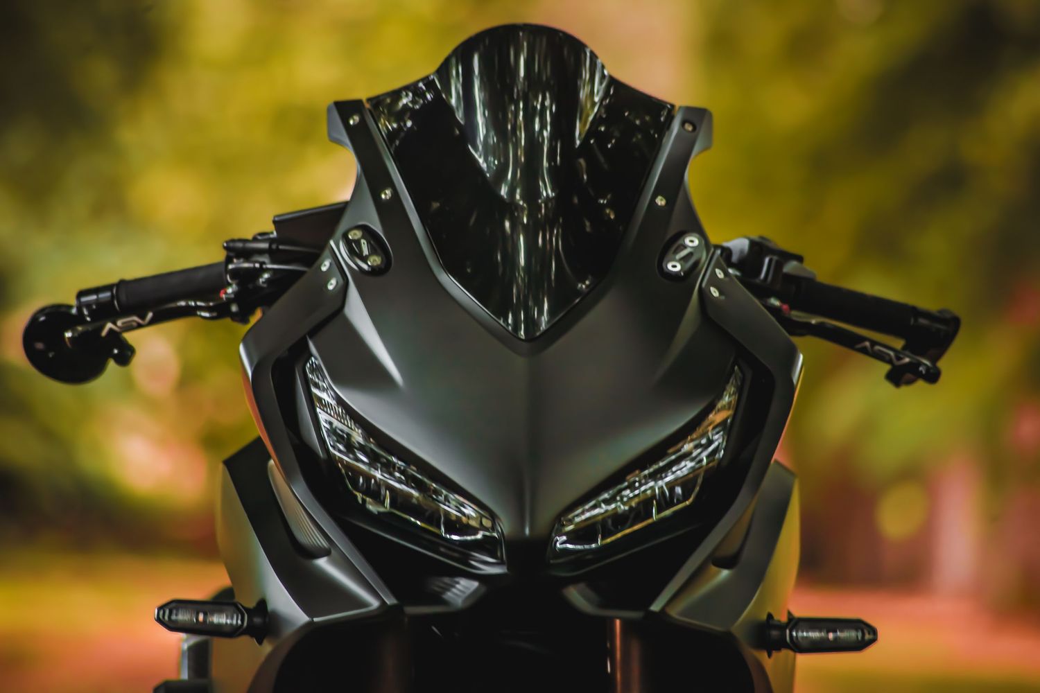 Black Ducati motorcycle with LED headlights shown in close-up detail against blurred autumn background.