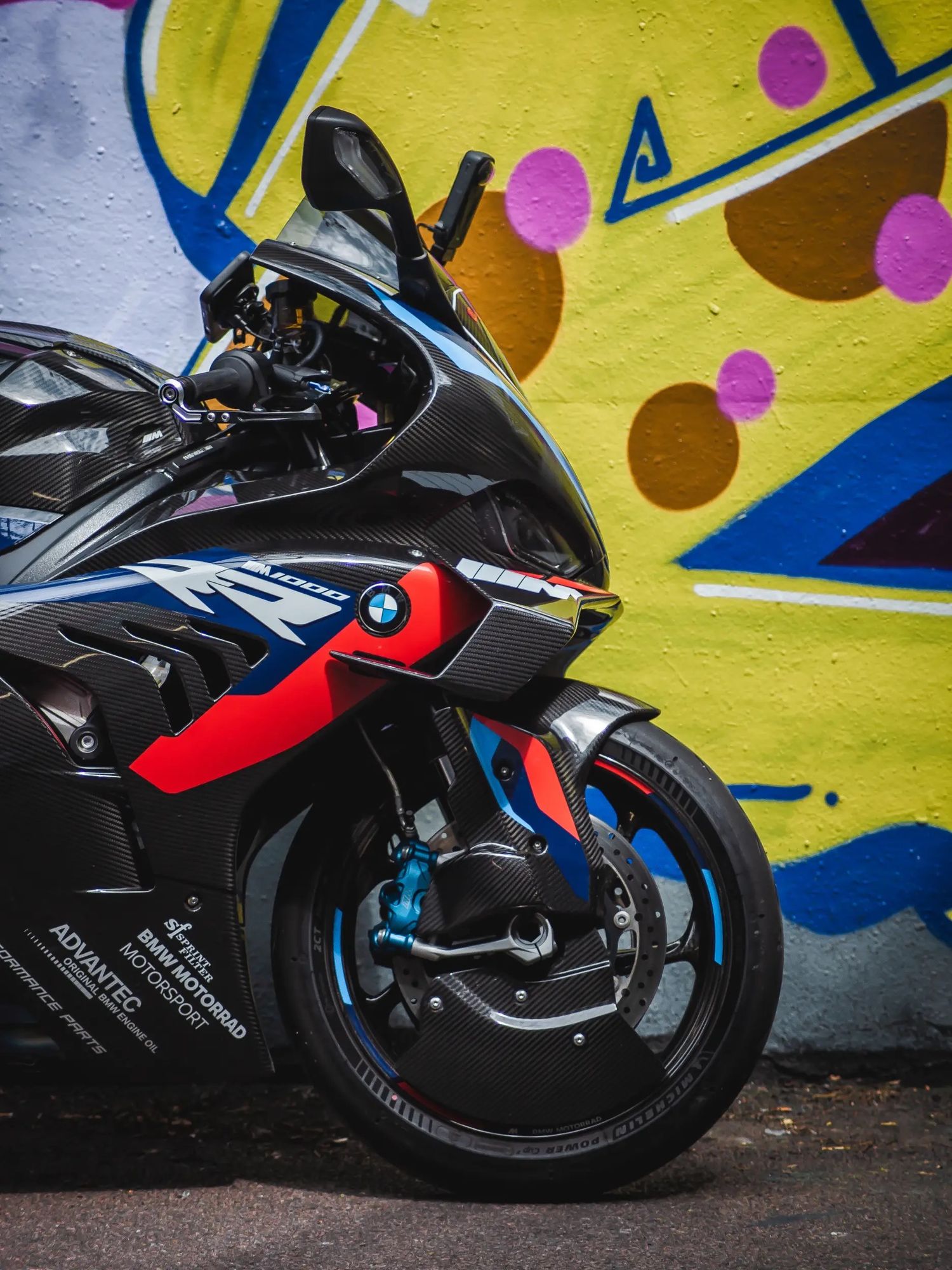 A black and red sports motorcycle parked against a colorful graffiti wall with yellow background and geometric shapes.