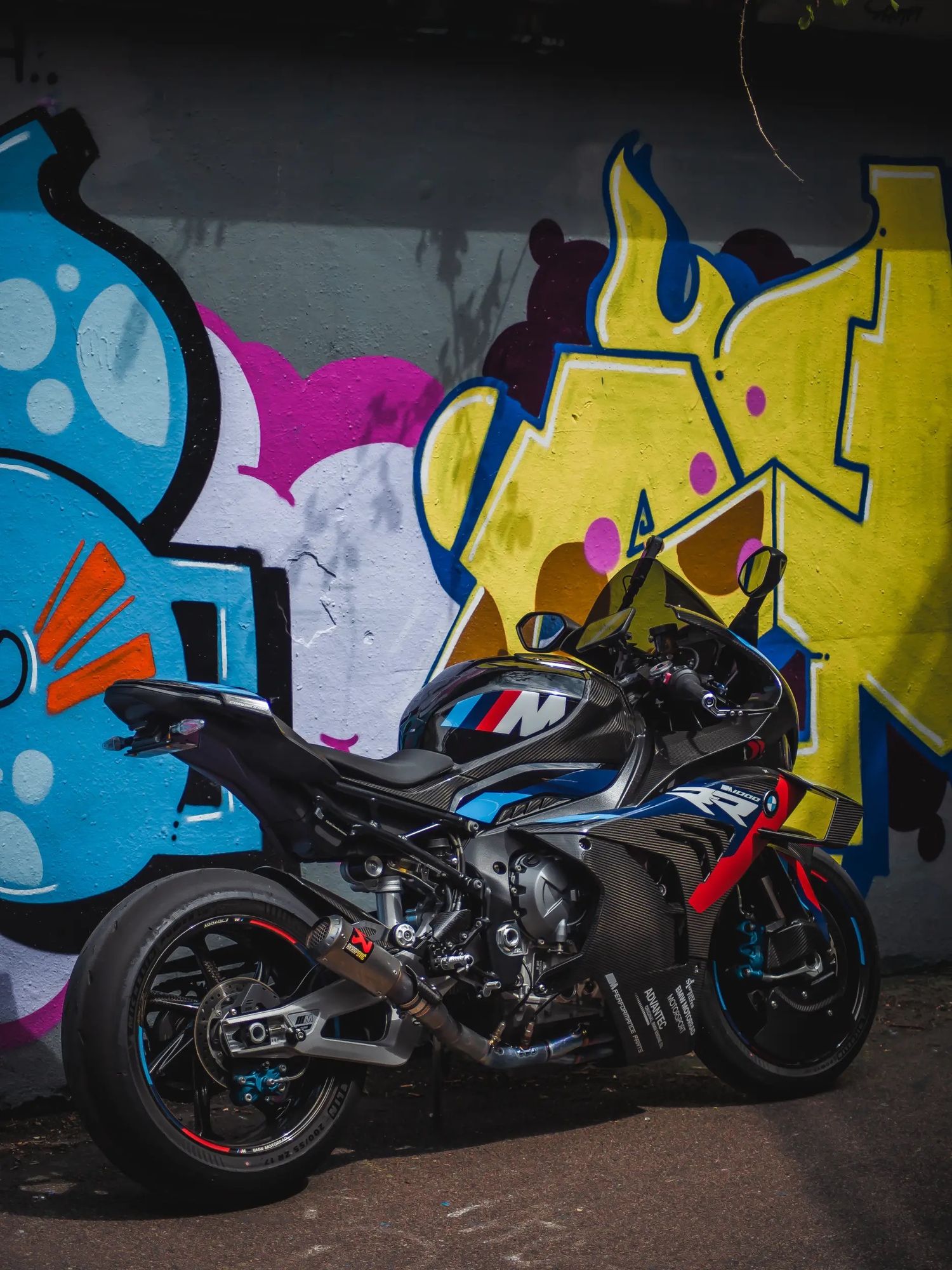 Black custom motorcycle parked against colorful graffiti wall with yellow and blue street art designs.