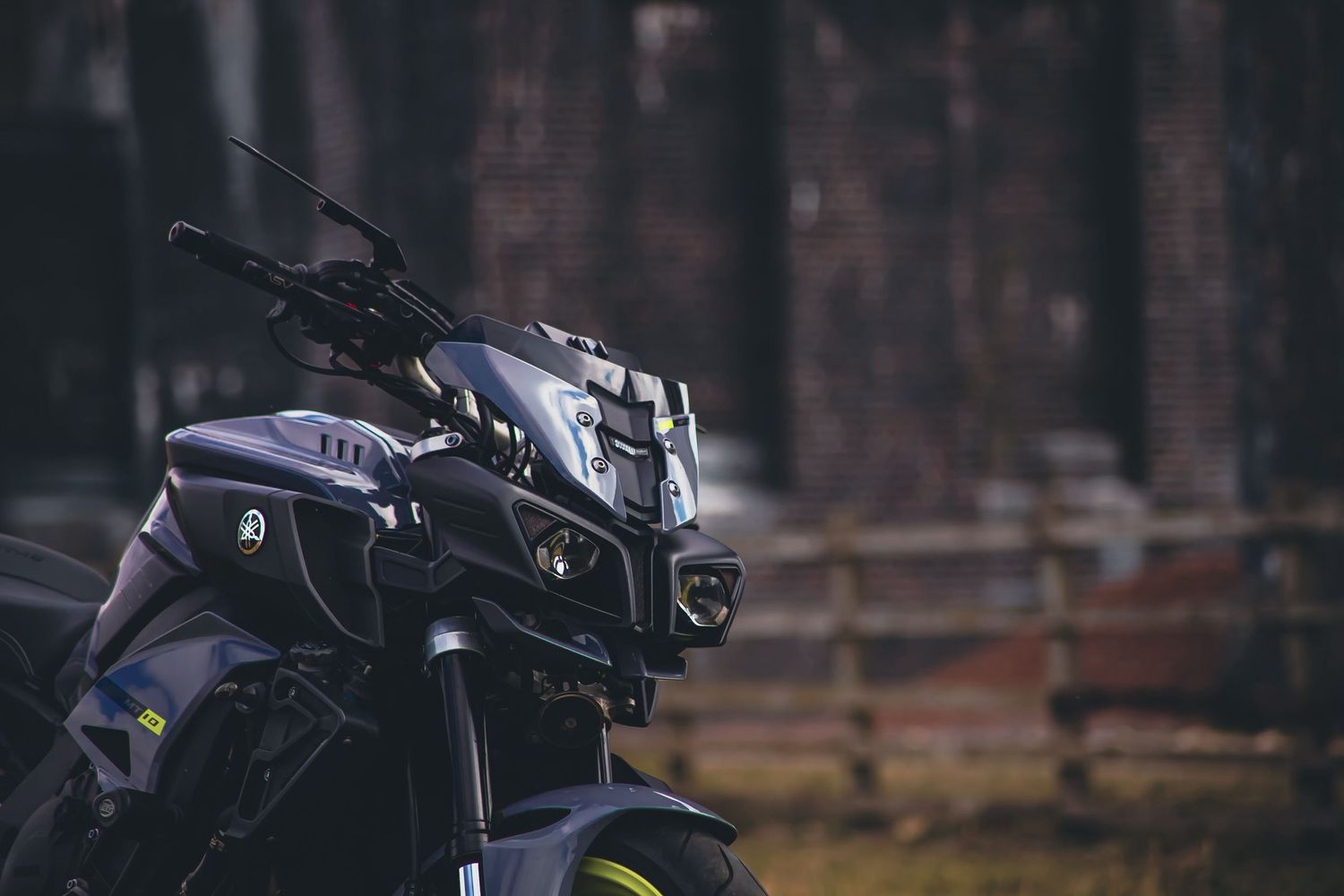 A sleek black motorcycle parked in a wooded area with autumn foliage in the background.