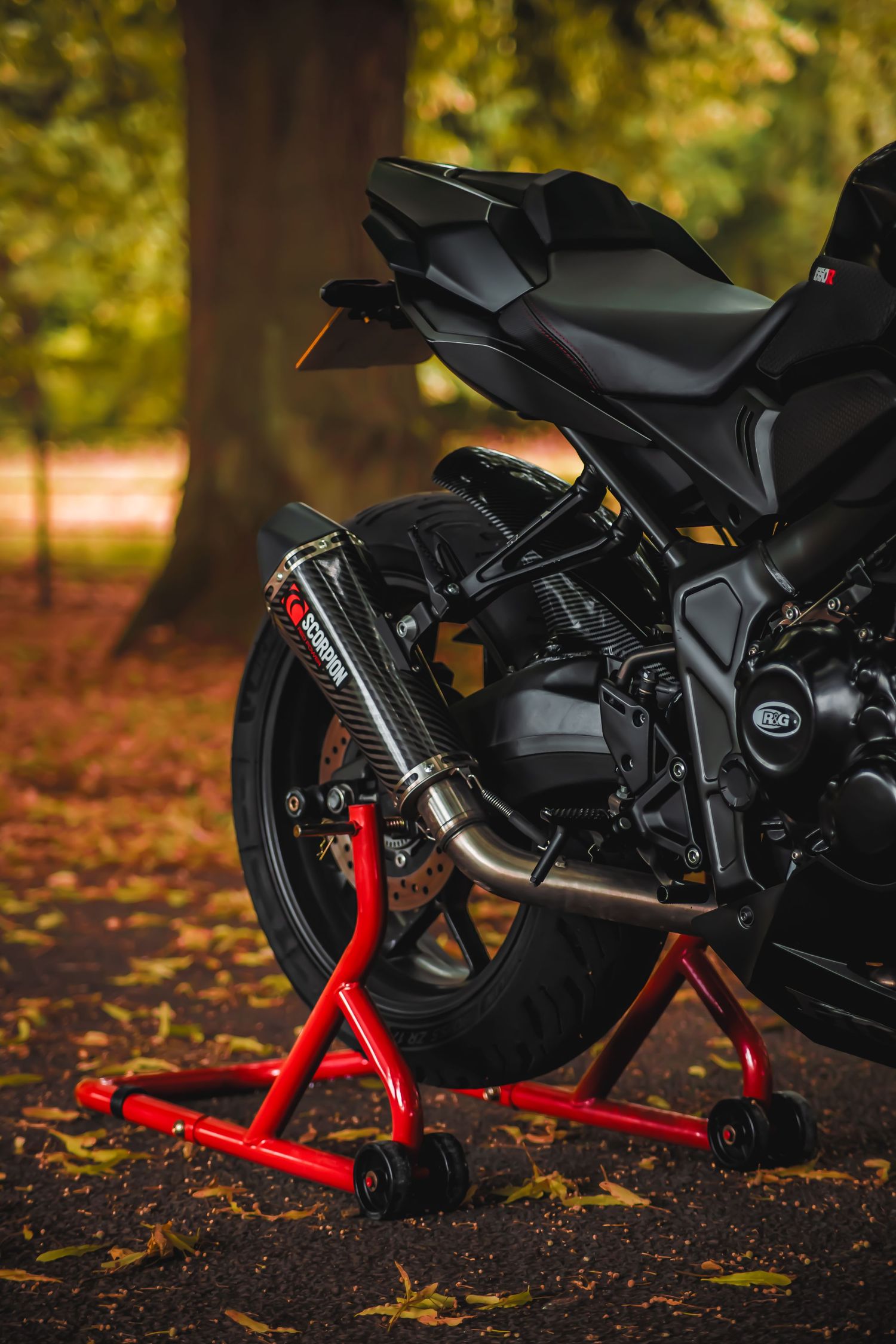 Close-up shots of a black motorcycle with red stand parts on autumn ground covered with fallen leaves.
