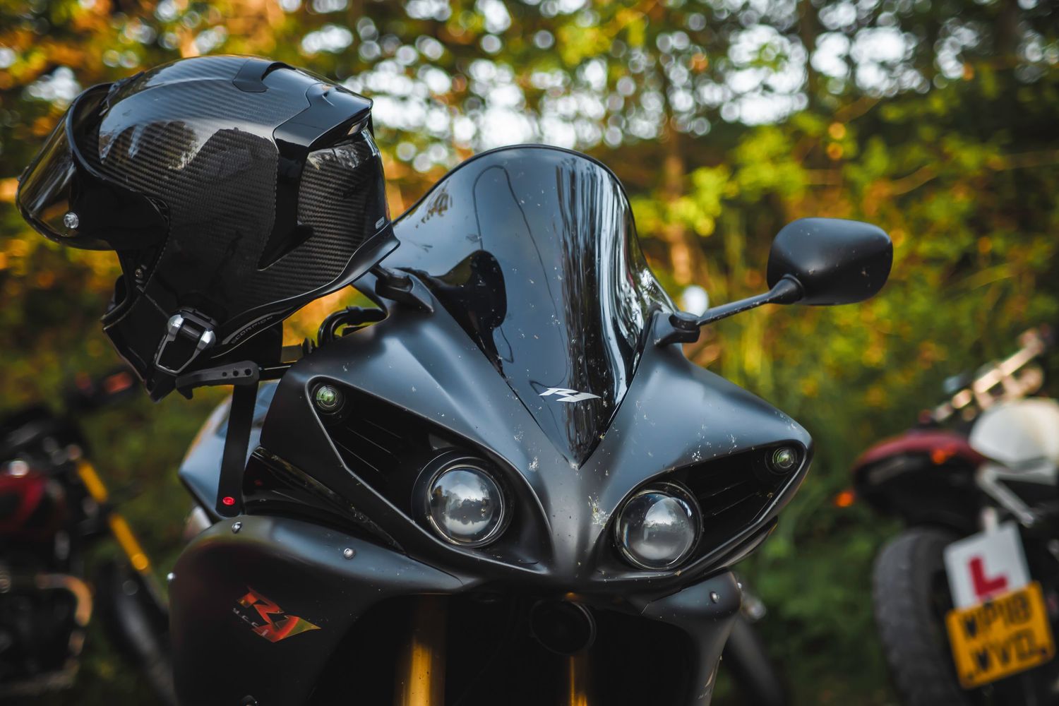 Close-up of a sleek matte black sports motorcycle front fairing with dual headlights against blurred autumn background.
