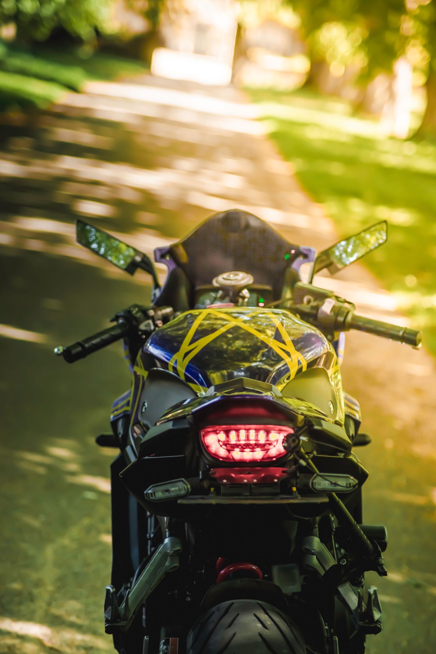 Close-up view of a motorcycle's rear LED tail light against a blurred natural background.