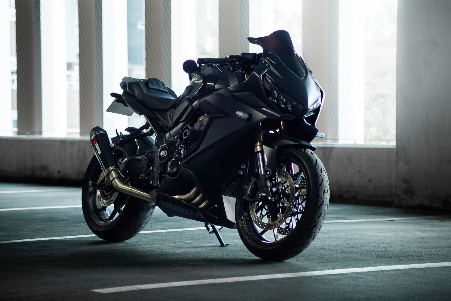 A sleek black motorcycle parked in a dimly lit concrete parking garage with white stripes on the floor.