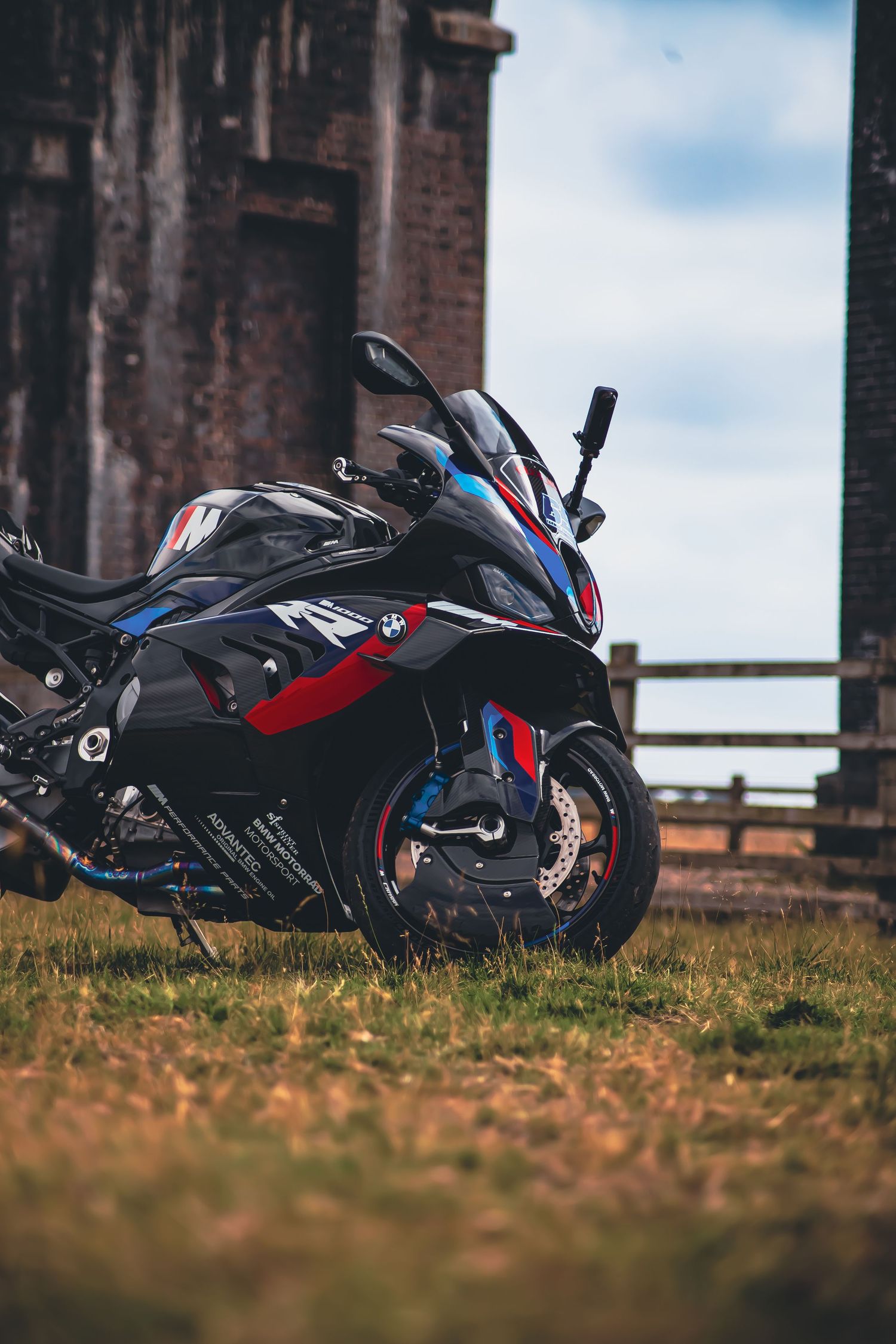Black BMW sport motorcycle parked on grass against stone building with dramatic angled composition showing multiple views.