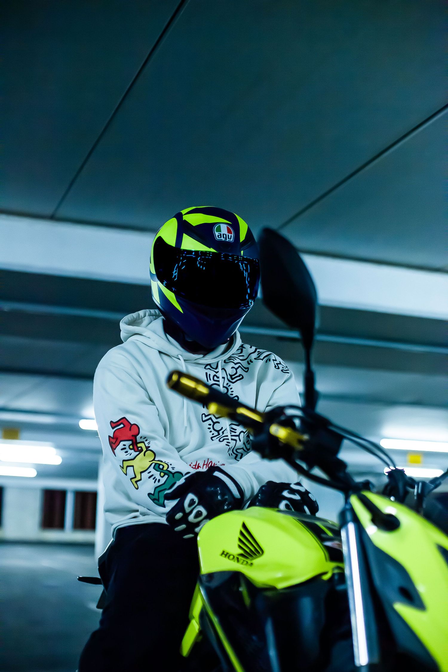 Motorcyclist in white hoodie riding a neon yellow sport bike in a dimly lit parking garage.