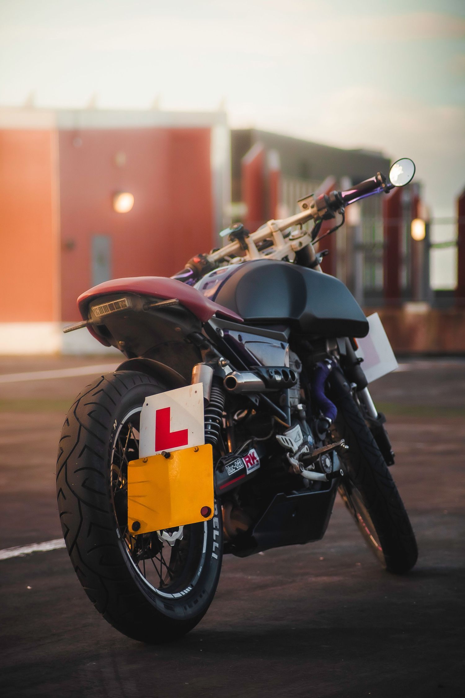 Custom motorcycle with learner plates photographed from multiple angles at sunset showing its sleek black and red design.