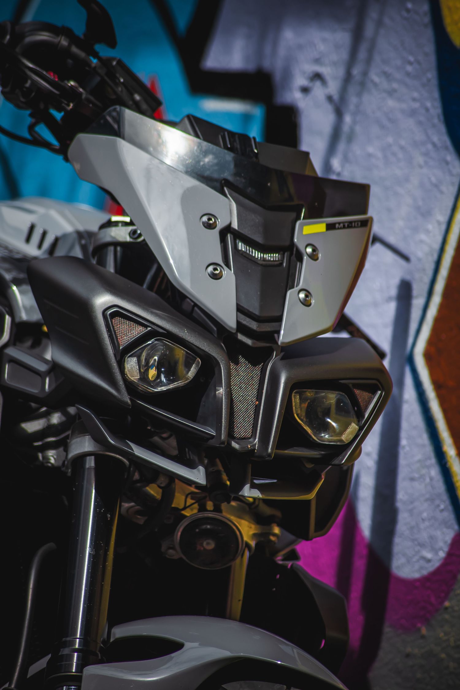 Modern motorcycle headlight assembly with angular design features and LED lighting against blue background.