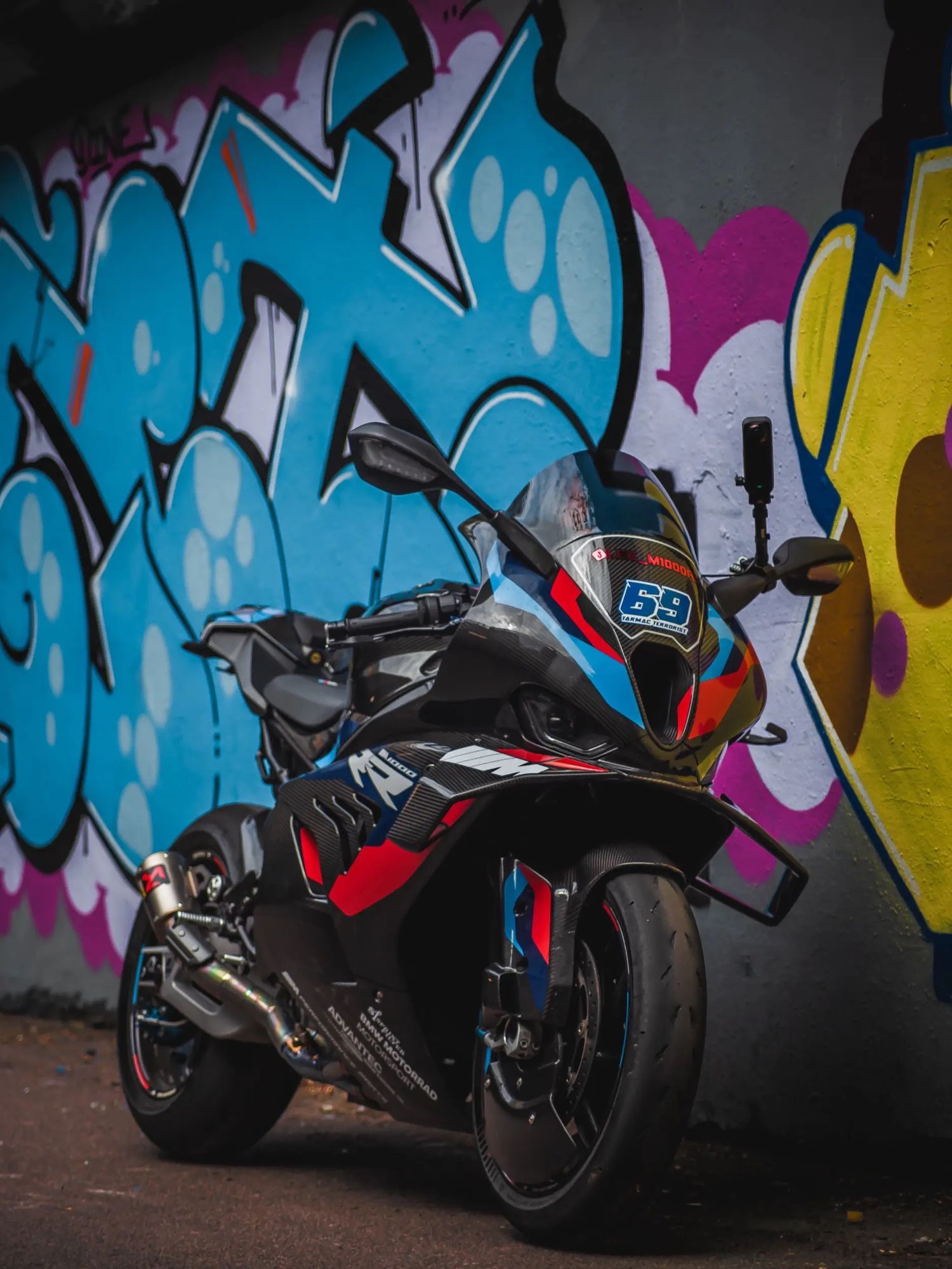 Black sports motorcycle parked against vibrant blue and pink graffiti wall showcasing sleek design and performance styling.