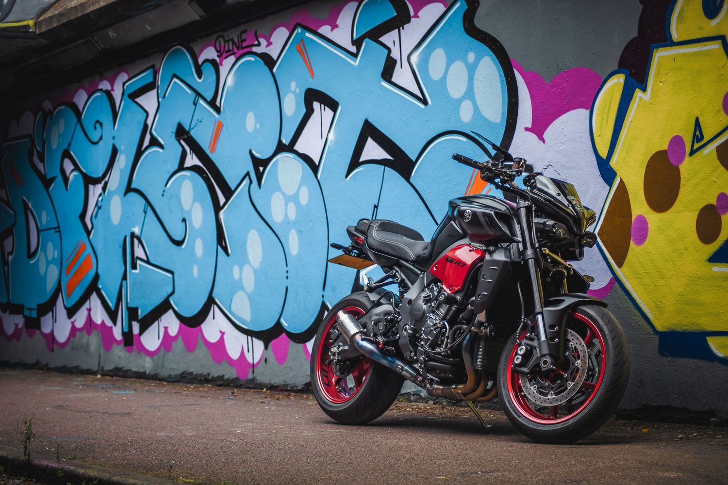Motorcycle parked against colorful graffiti wall featuring bright blue street art.