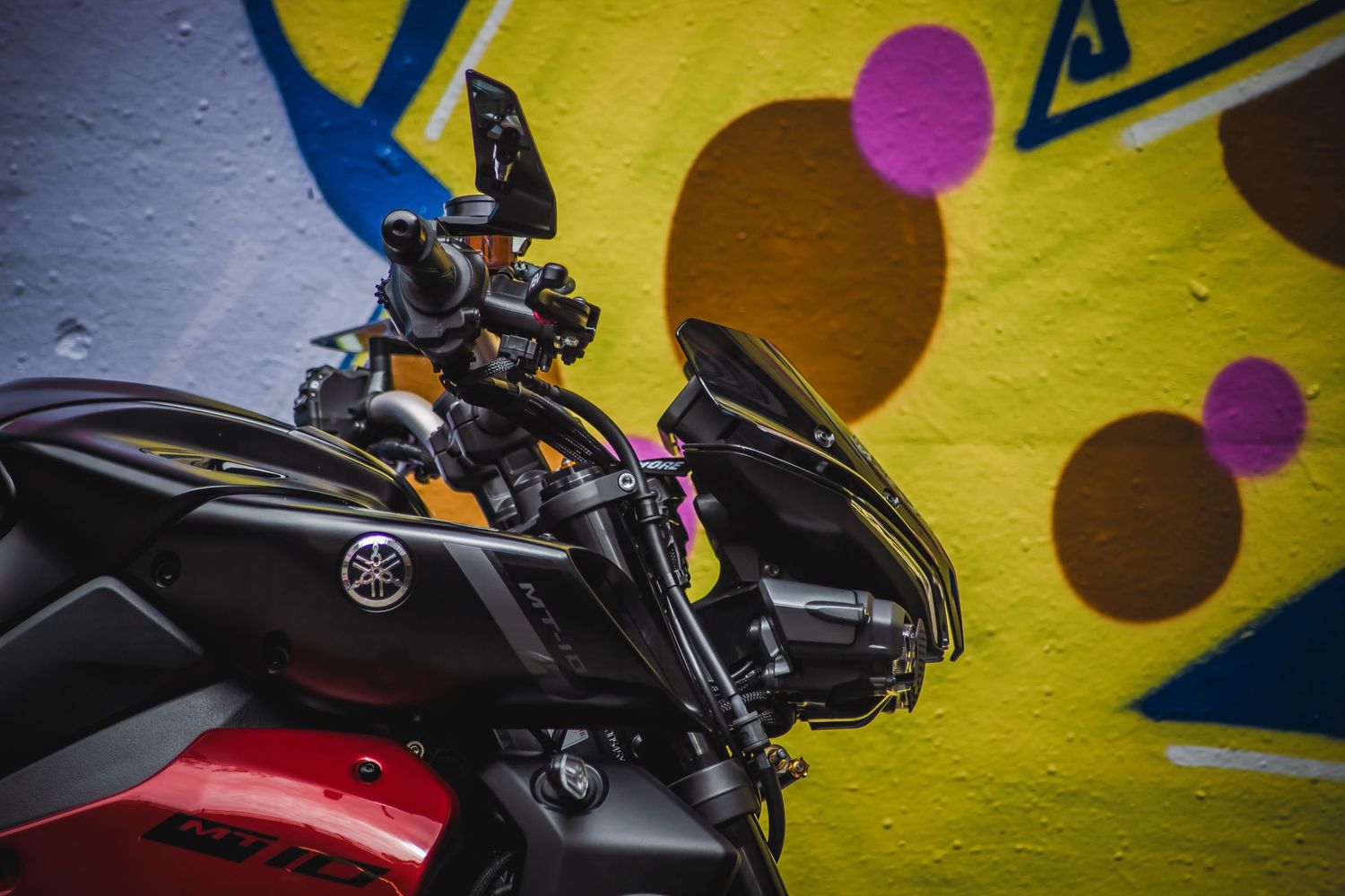 Sleek black motorcycle silhouette against a vibrant yellow wall with colorful circular patterns.