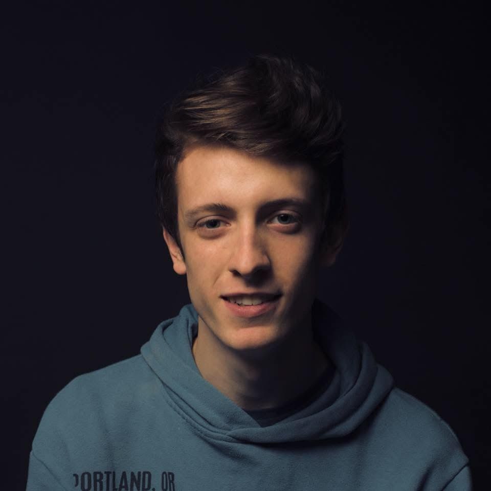 Portrait of a young man in a blue hoodie against dark background.