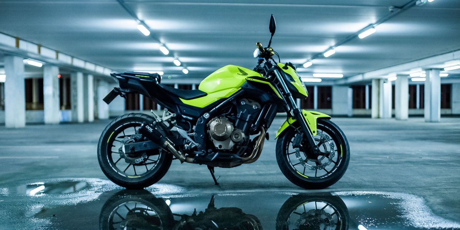 Sleek black motorcycle parked in a dimly lit concrete parking garage with fluorescent lighting overhead.