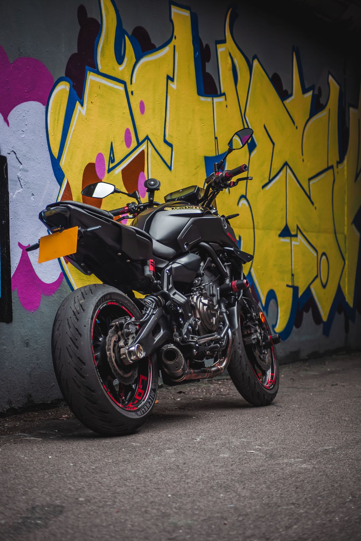 Custom black motorcycle photographed against a vibrant yellow graffiti wall in an urban setting.