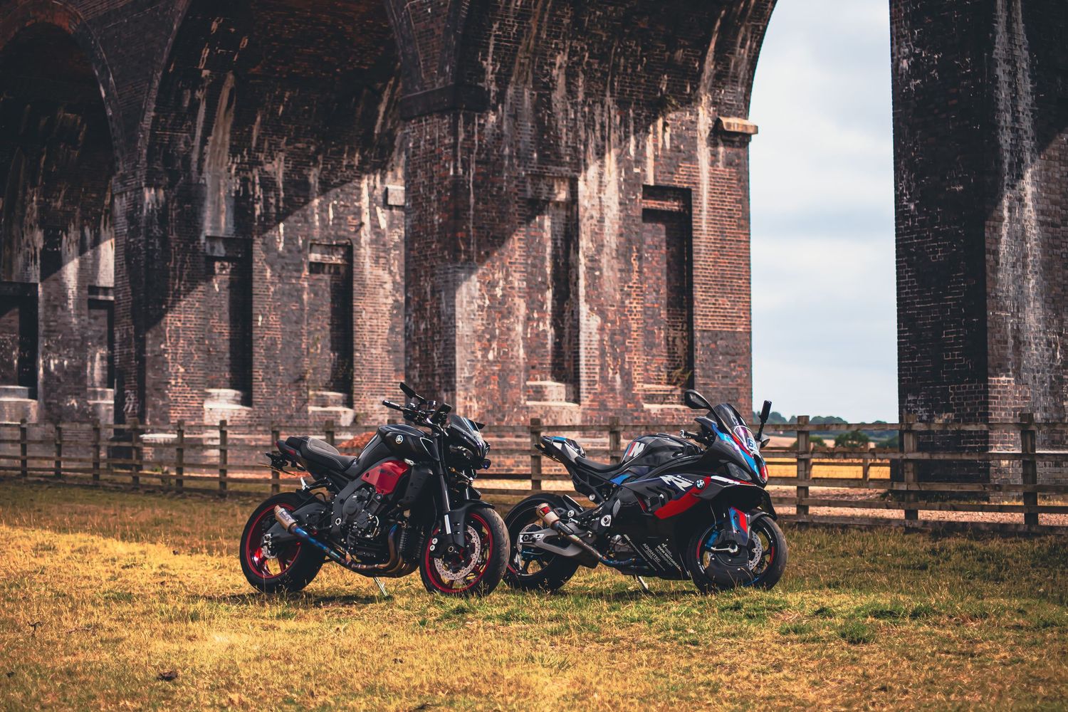 Black sport motorcycles lined up against a rustic brick building backdrop.