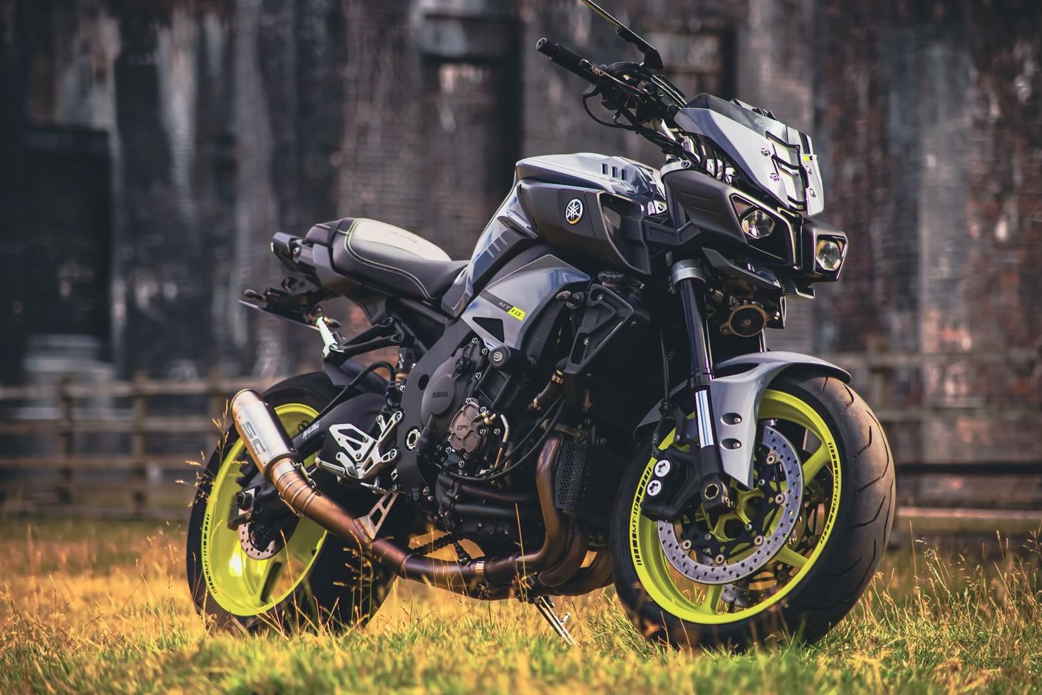 A sleek black motorcycle with neon green accents parked against a rustic brick wall background.