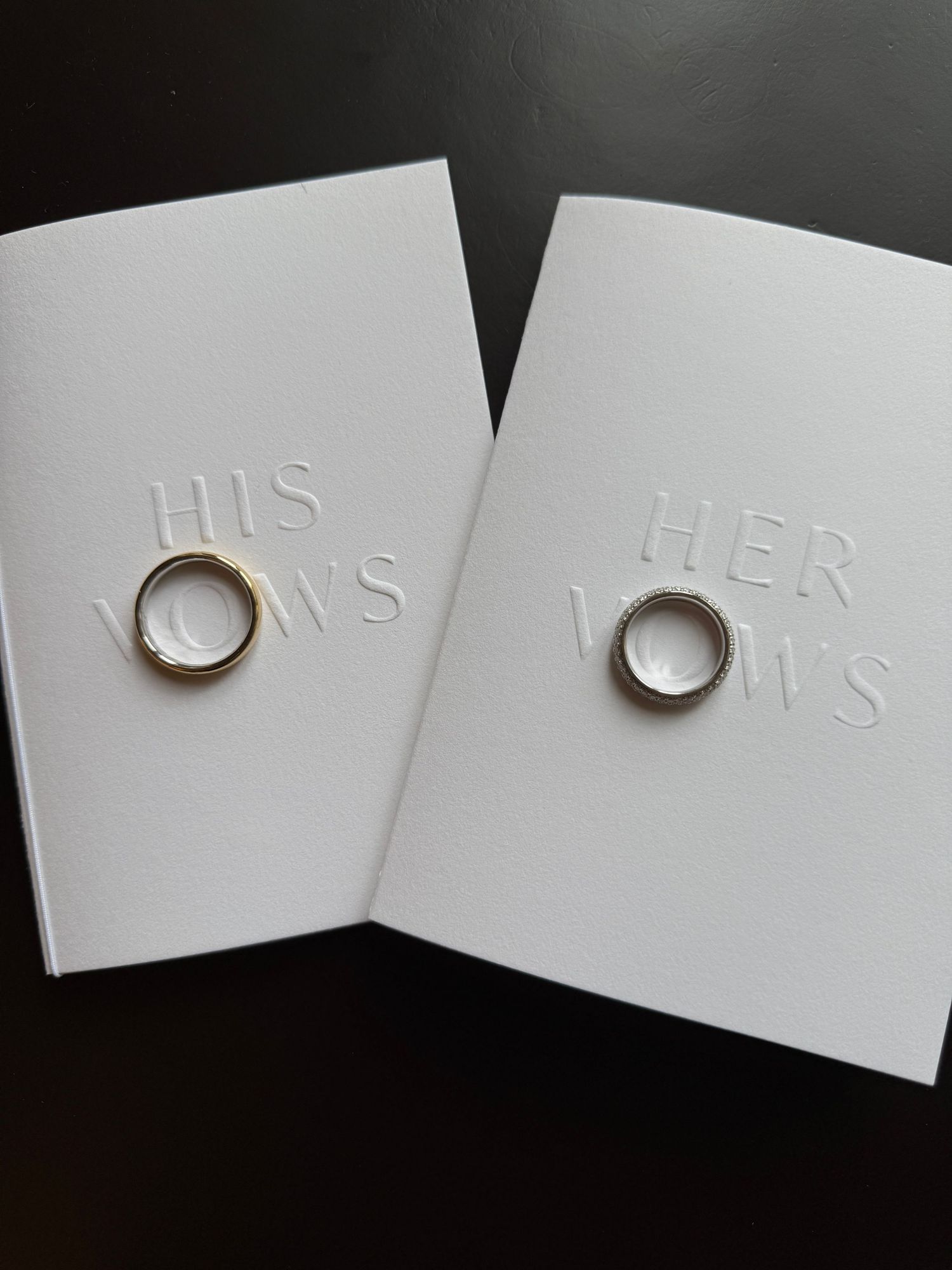 A close-up iPhone photo of two gold wedding bands resting on elegant vow booklets during a wedding in Tuscany. Captured by Behind Wed