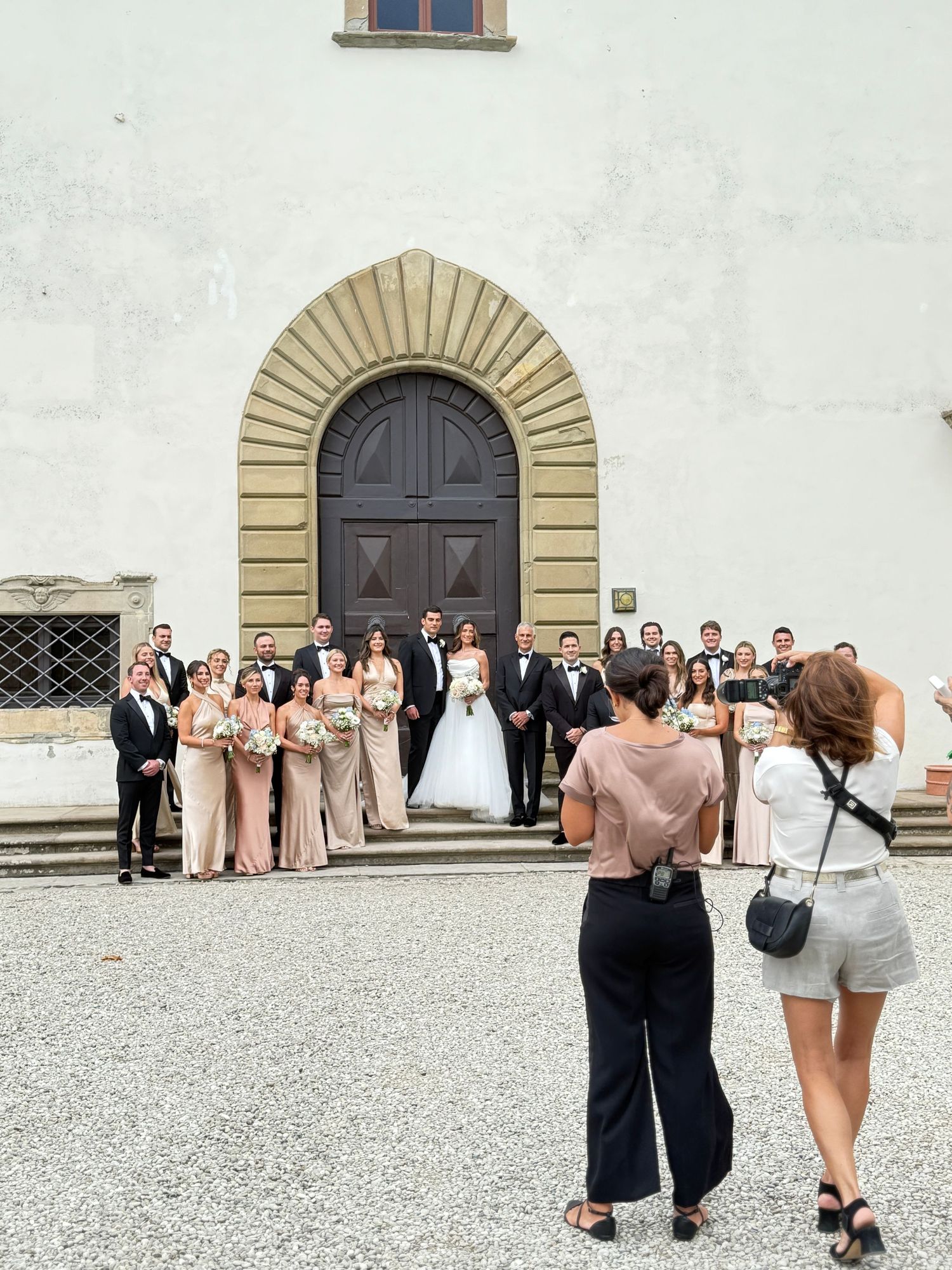 Wide-angle iPhone shot of a bride, groom, and their wedding party posing in front of an elegant historic estate in Tuscany, by Behind Wed