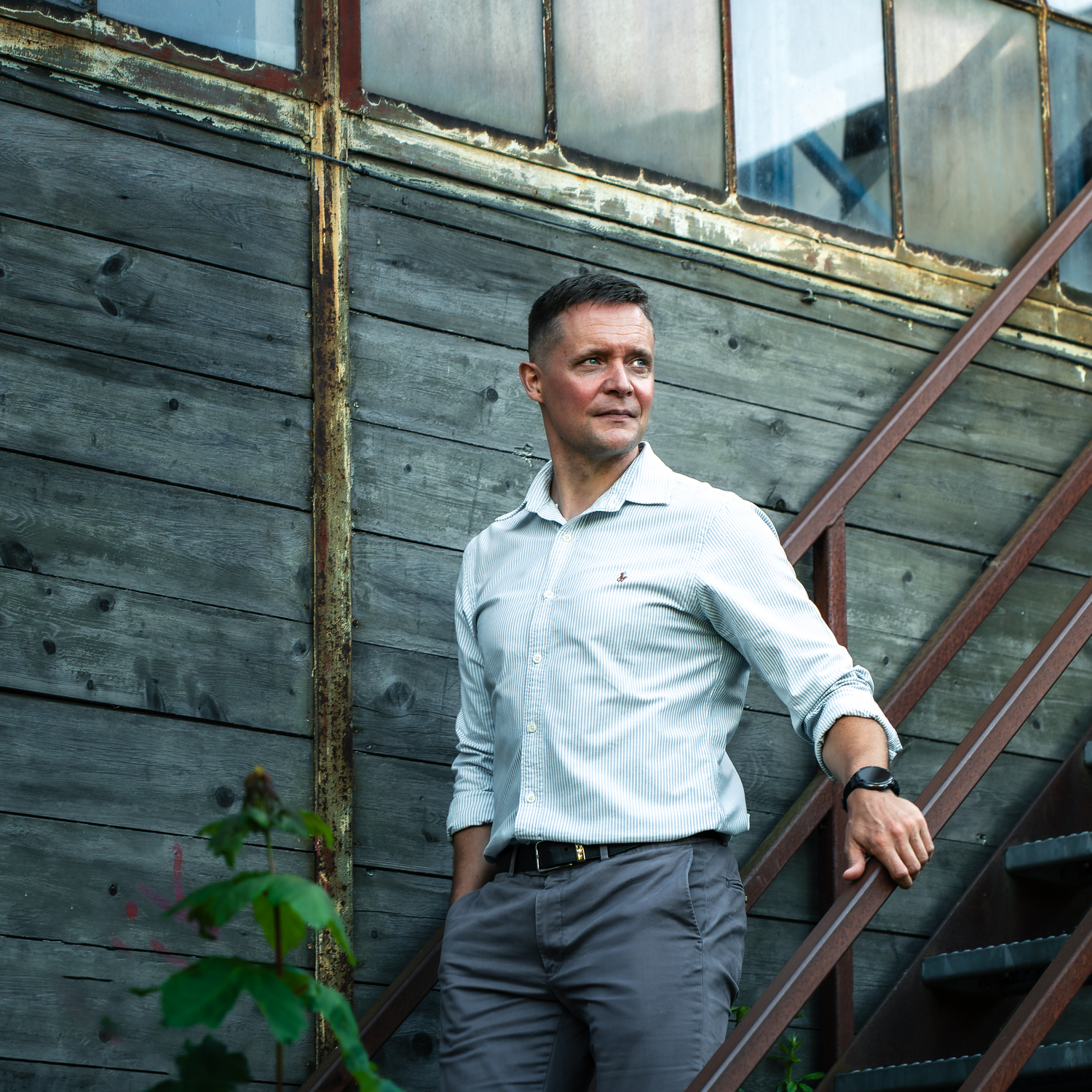 Person in white shirt standing by rustic wooden wall in outdoor setting.