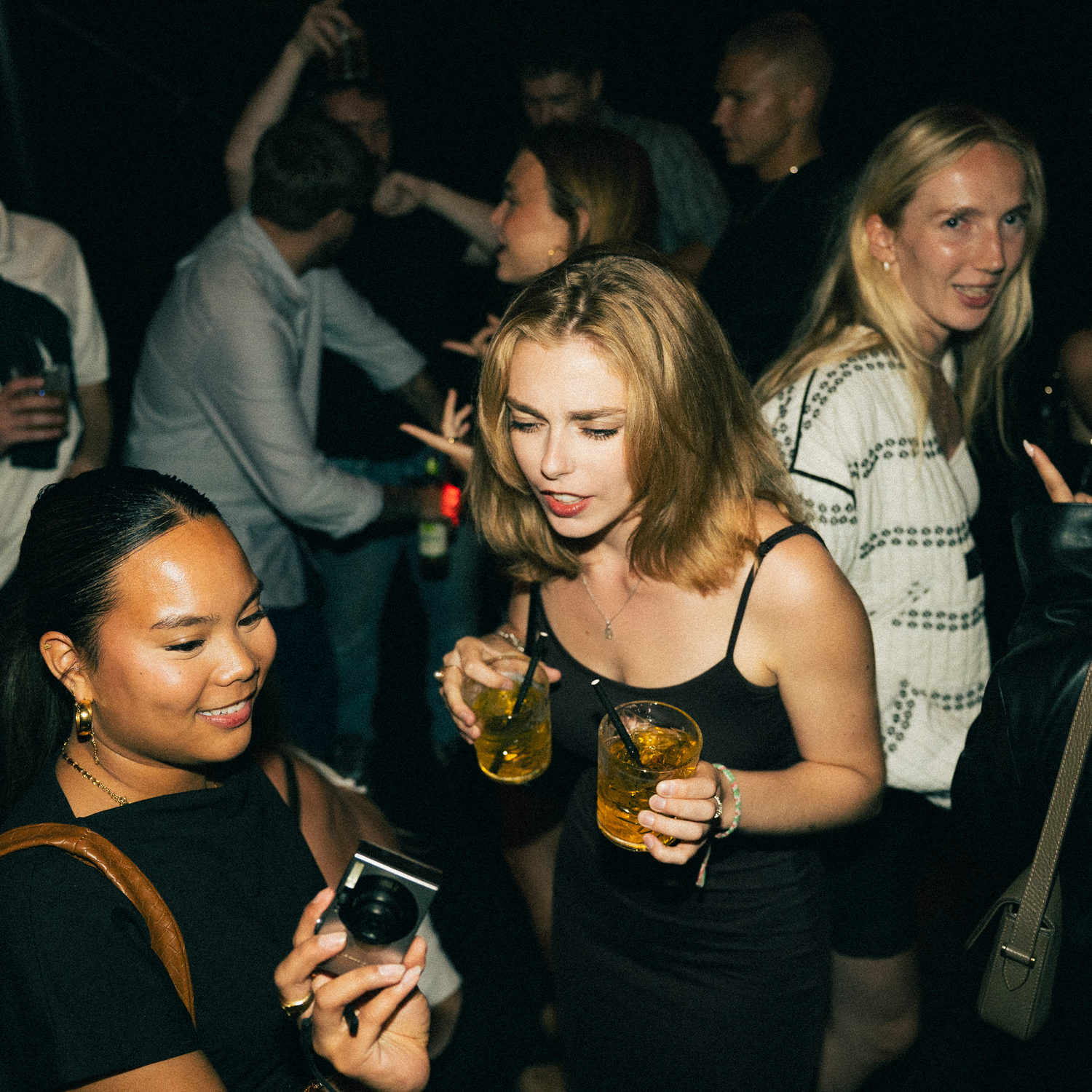 People socializing with drinks at a dimly lit nightclub venue with a vibrant party atmosphere.