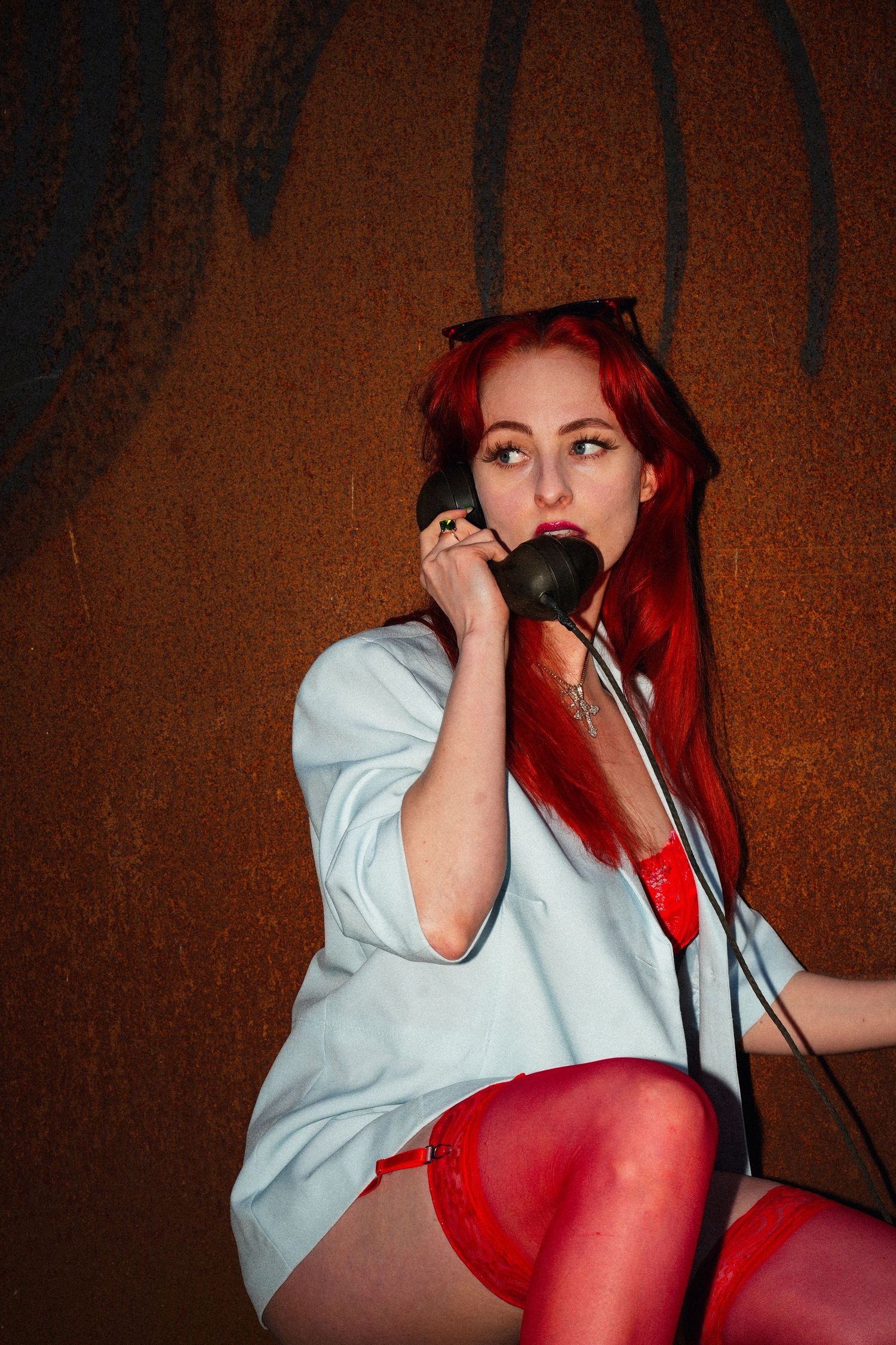 A performer with bright red hair in a white shirt and red stockings sits while holding a microphone in a dramatic pose.