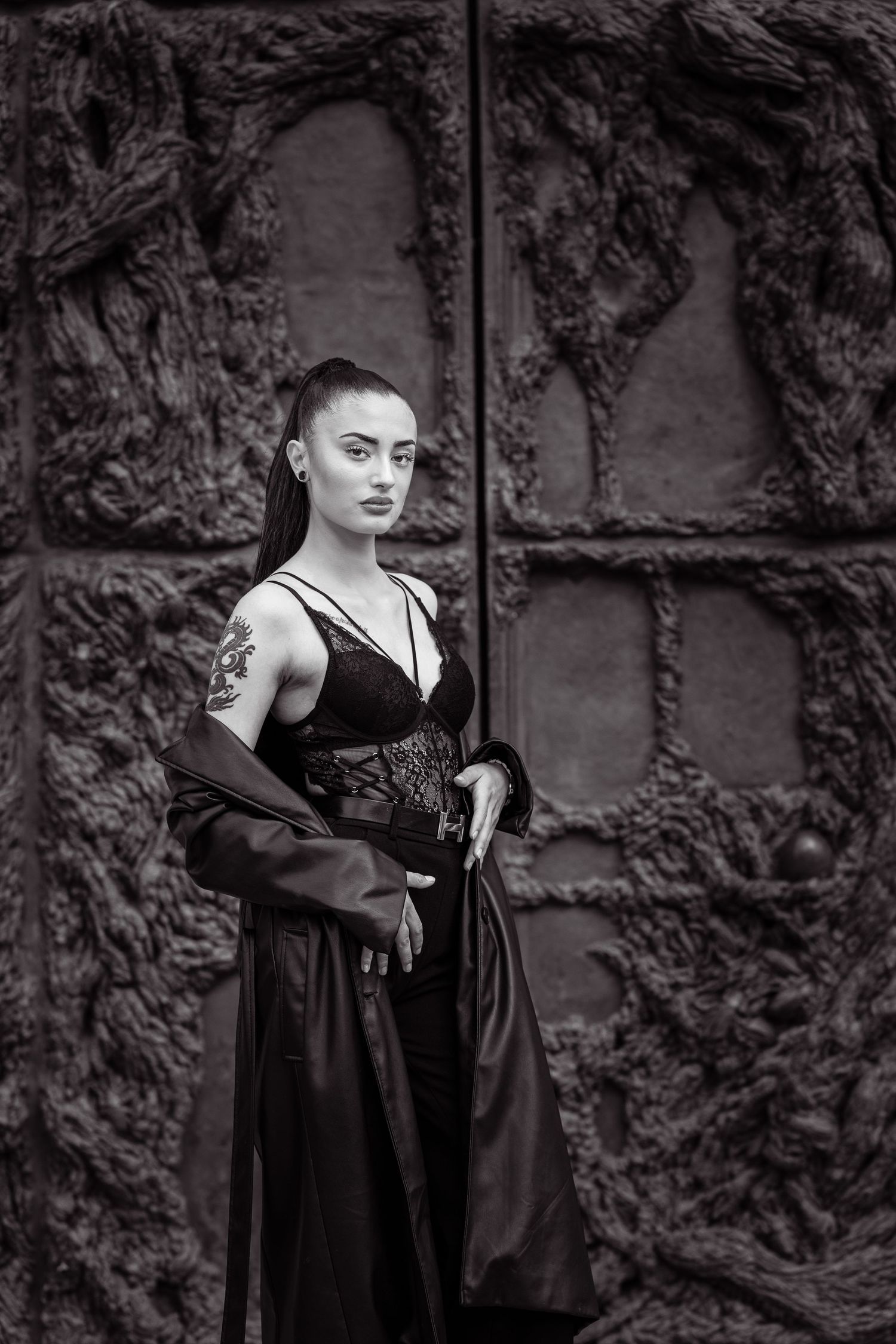 Black and white portrait of a woman in gothic Victorian-style dress with corset detail against a textured stone wall.