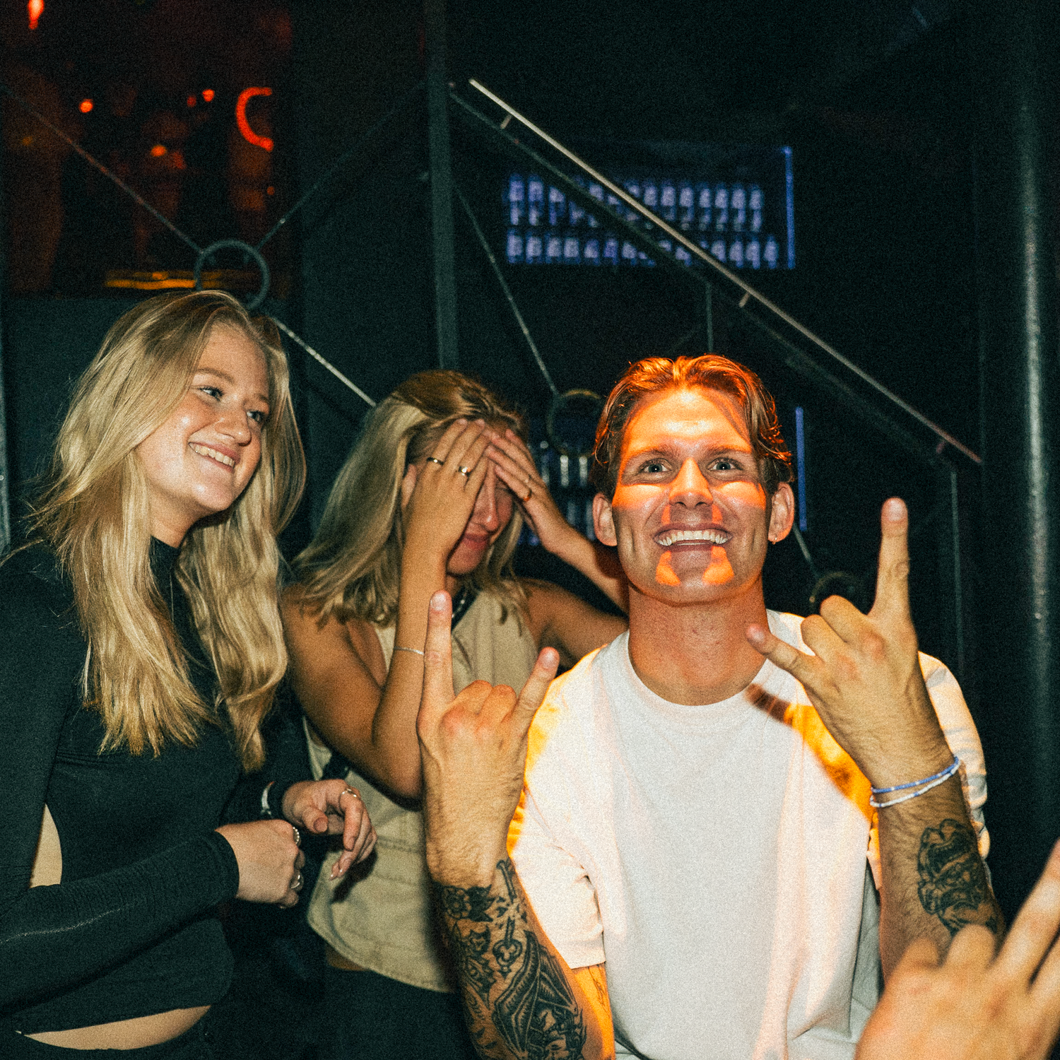 People enjoying a night out at a club or party with energetic smiles and hand gestures in dim lighting conditions.