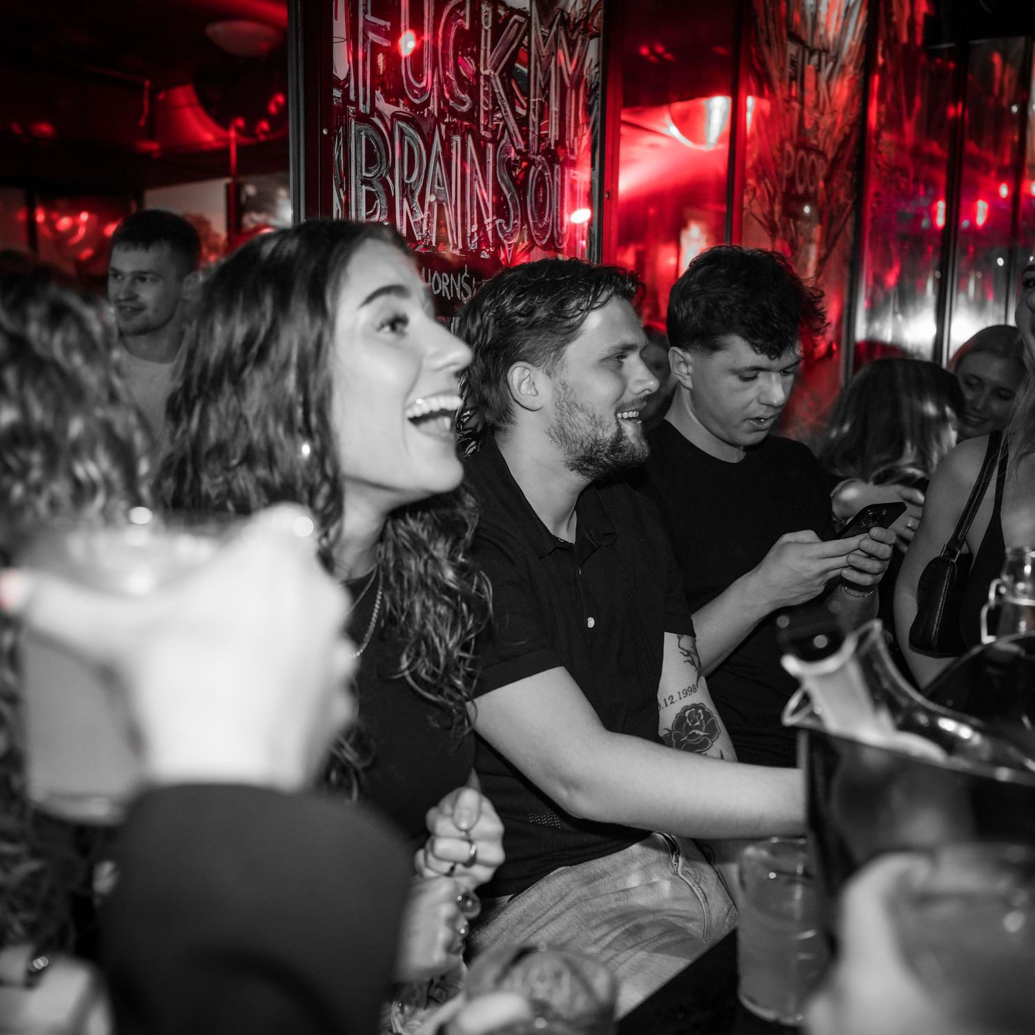 Crowd of young people enjoying a lively atmosphere at a nightclub with red lighting and black and white photography effect.
