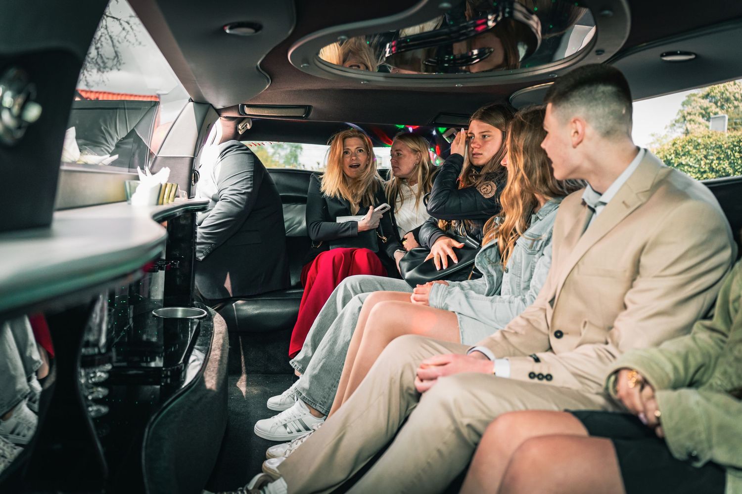 Group of friends sharing an animated conversation while riding together in the back of a luxury car.